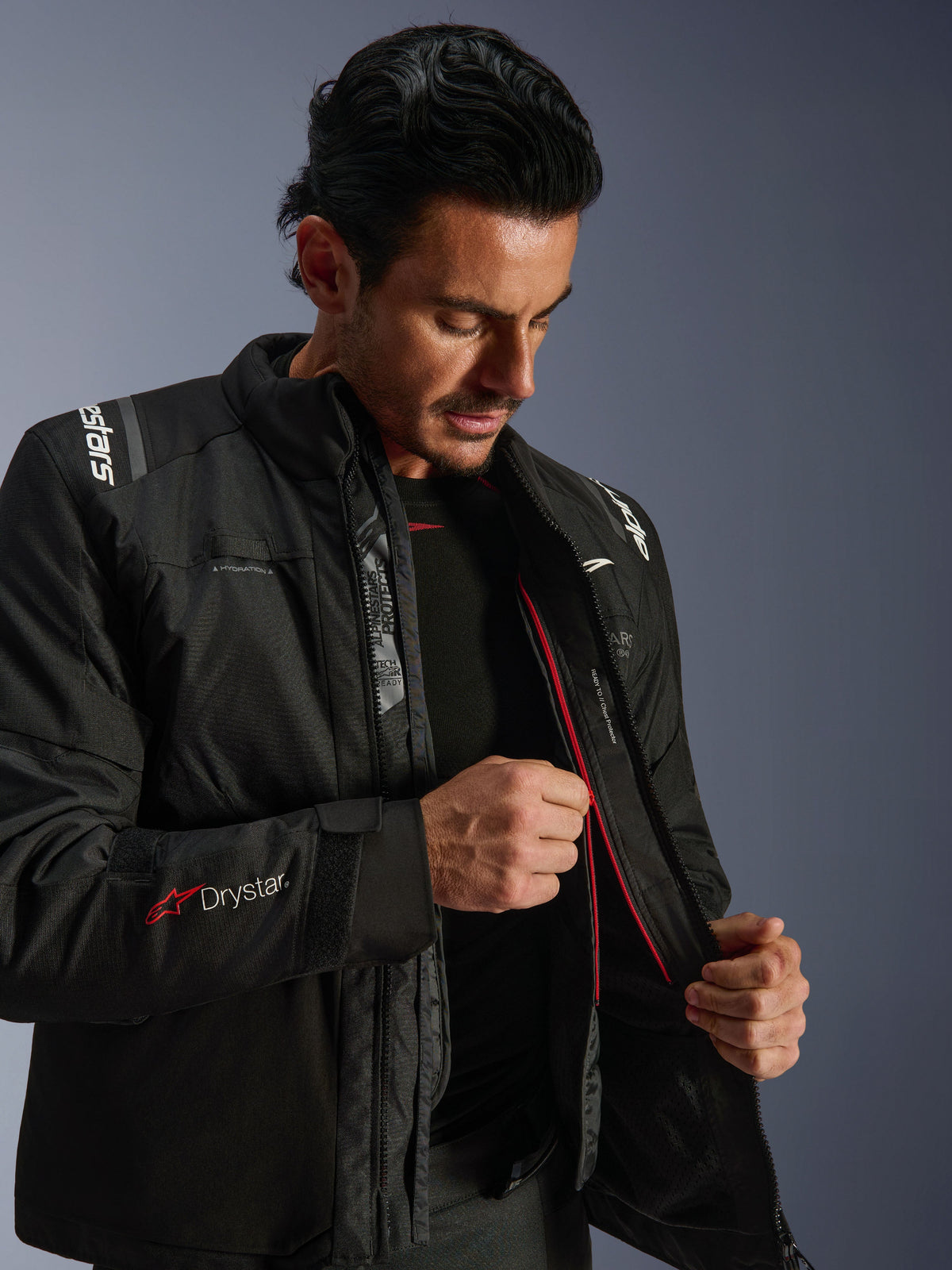 Alpinestars Andes V4 Drystar® Jacket, giacca da moto adventure nera, uomo che mostra la fodera termica interna e la cerniera rossa, con logo Drystar® sulla manica, materiale tessile resistente per la guida in ogni condizione atmosferica