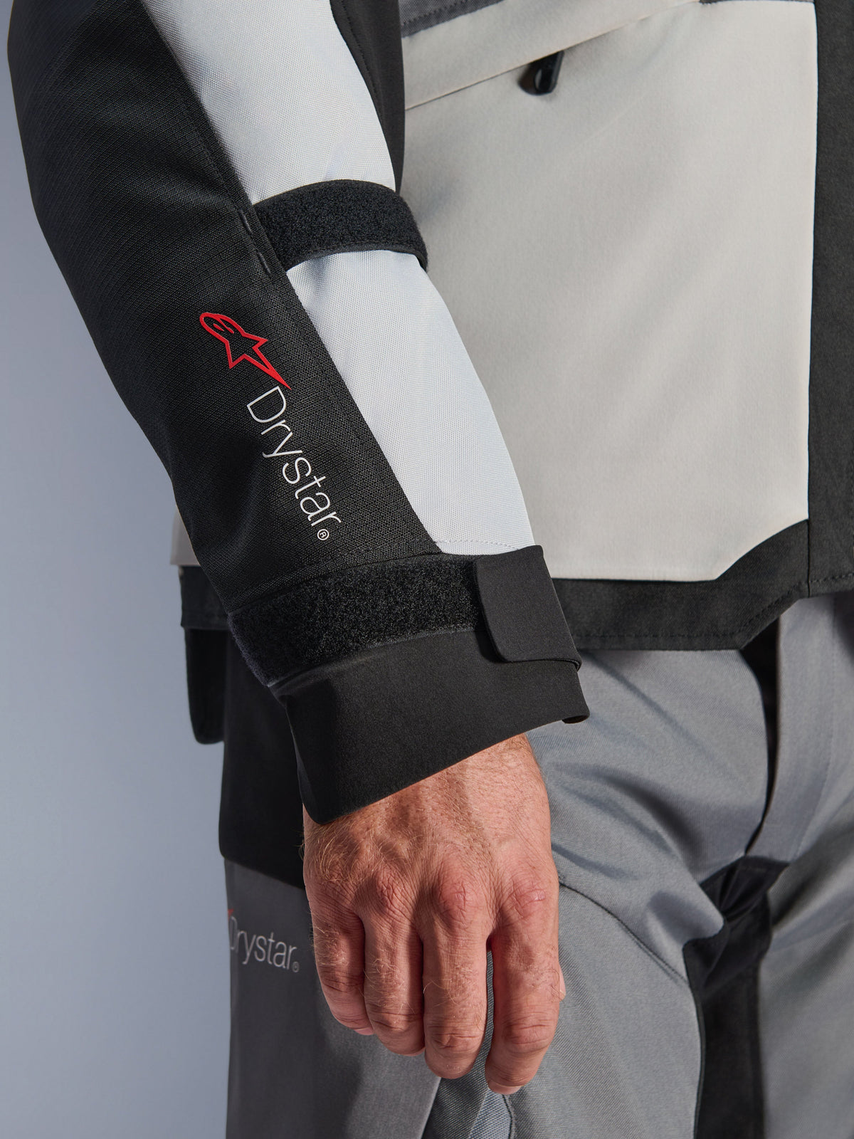Alpinestars Andes V4 Drystar® Jacket, giacca da moto adventure, pannelli grigio ghiaccio e neri, primo piano della manica con logo Drystar® rosso e cinghie regolabili, design in tessuto funzionale per la guida con ogni condizione atmosferica