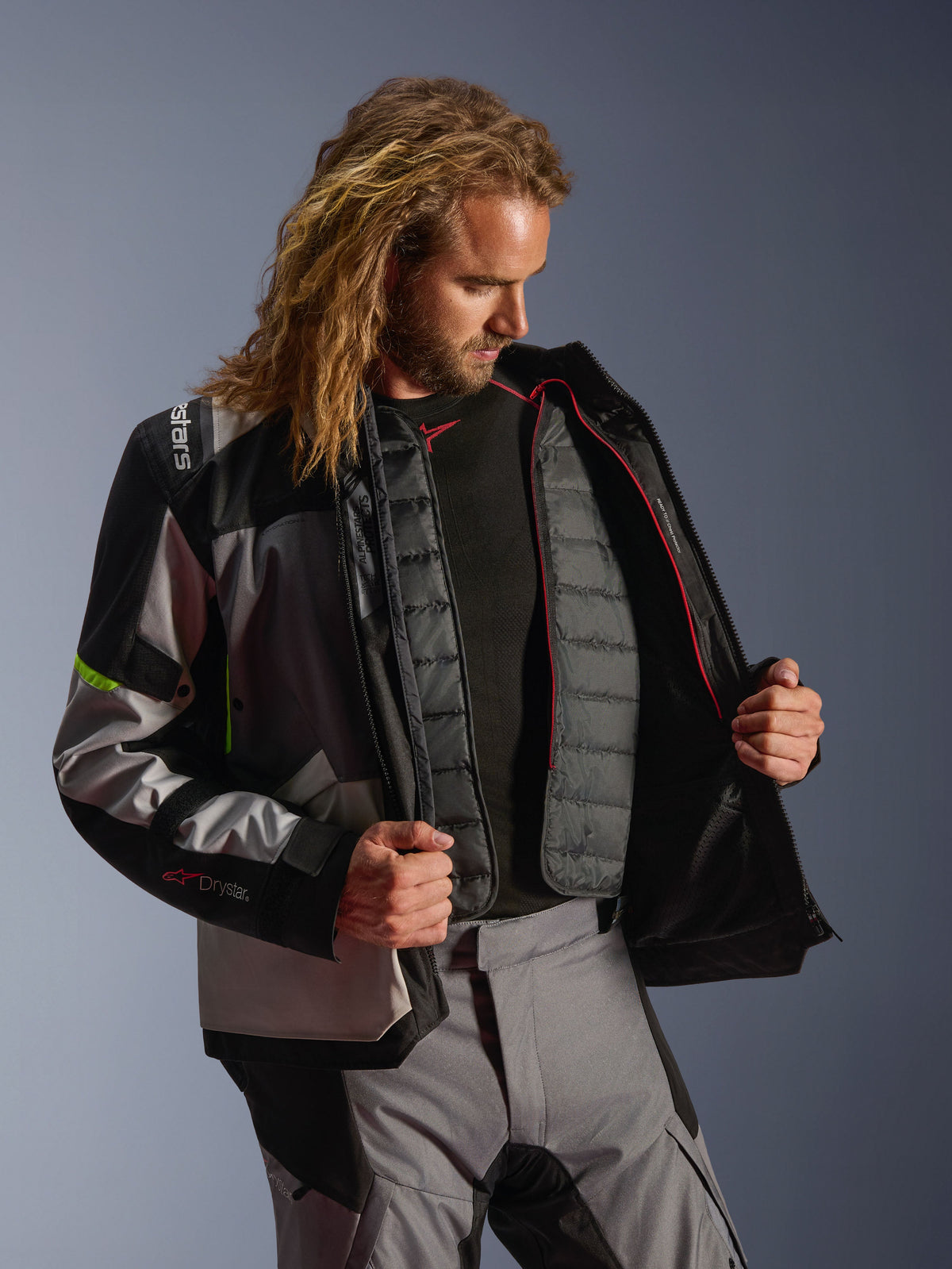 Giacca Alpinestars Andes V4 Drystar®, abbigliamento da moto adventure in grigio scuro, grigio ghiaccio e giallo fluo, modello maschile che mostra la fodera termica interna trapuntata, indossata con pantaloni coordinati, design per prestazioni in tutte le condizioni atmosferiche