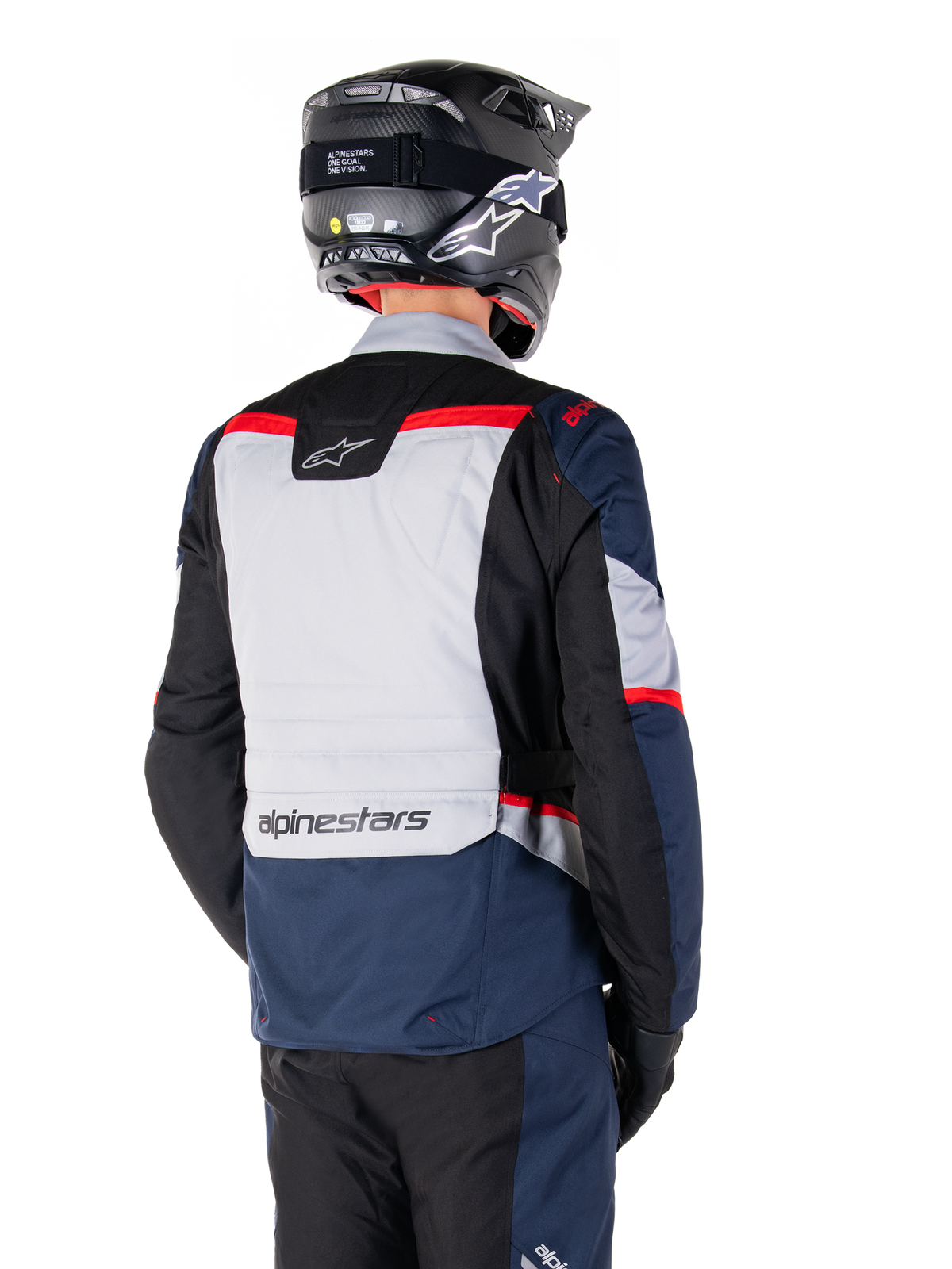 Giacca Alpinestars ST-1 Waterproof, blu scuro, nero e rosso brillante, vista posteriore su un pilota con casco da adventure nero, caratterizzata da pannelli grigio chiaro e logo Alpinestars, abbigliamento da moto adventure touring