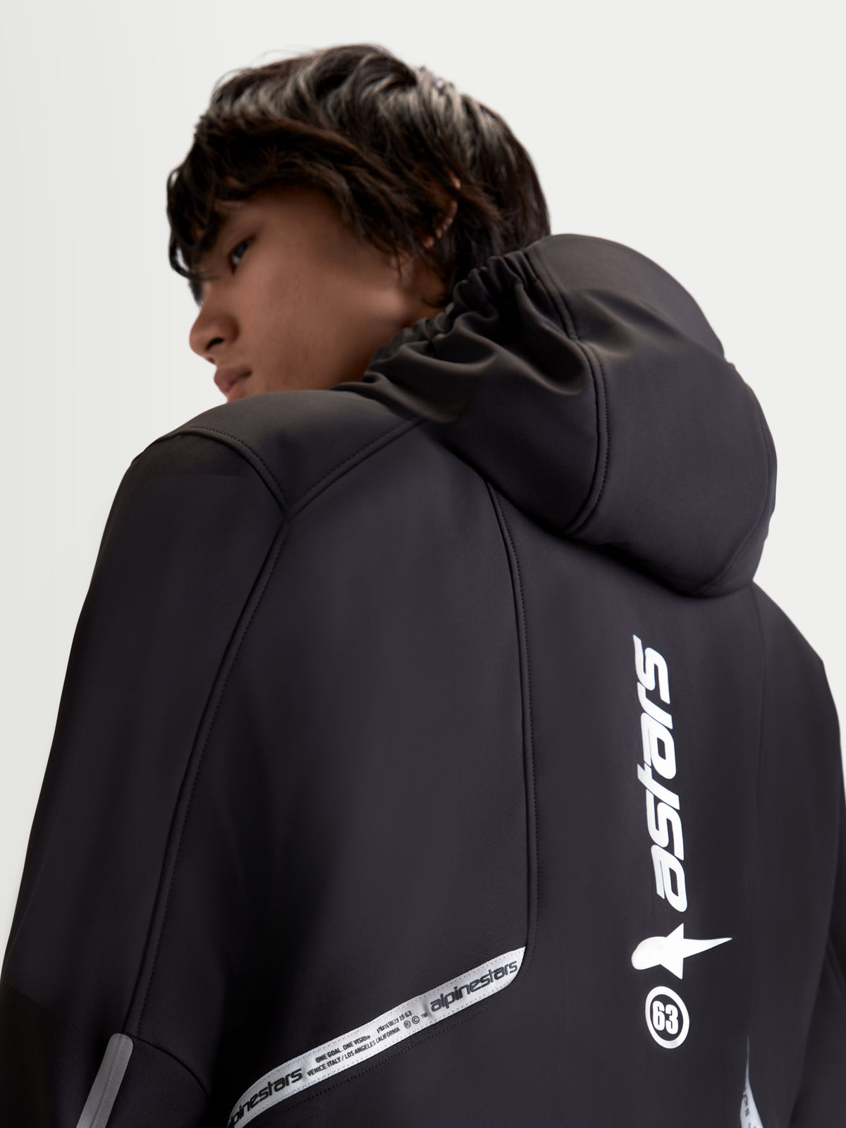 Alpinestars C 5 Drystar Giacca, giacca da moto urbana contemporanea da uomo in colore nero, vista posteriore ravvicinata che mostra il cappuccio integrato e i dettagli del marchio riflettenti indossati da un modello