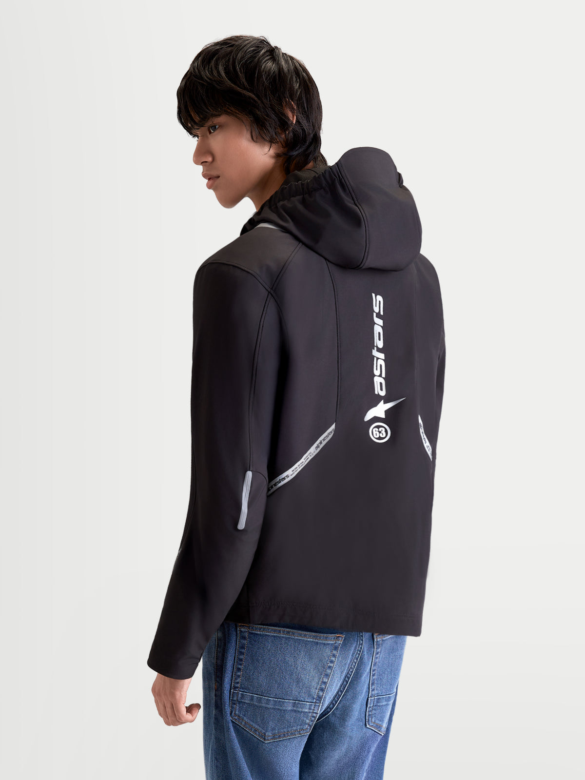 Alpinestars C 5 Drystar Giacca, giacca da moto urbana contemporanea da uomo in nero, vista posteriore di tre quarti su un modello con cappuccio integrato, dettagli riflettenti e logo verticale stampato sulla schiena