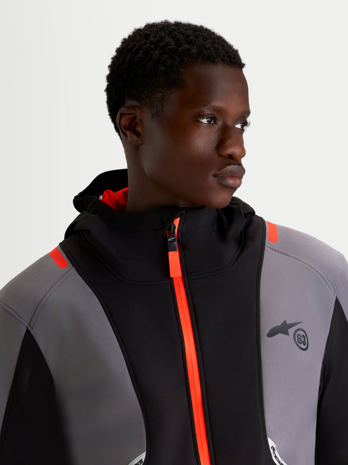 Alpinestars C 5 Drystar Giacca, giacca da moto urbana da uomo in nero e grigio scuro, vista in primo piano su un modello che indossa la giacca softshell impermeabile con cerniera frontale arancione brillante e cappuccio integrato