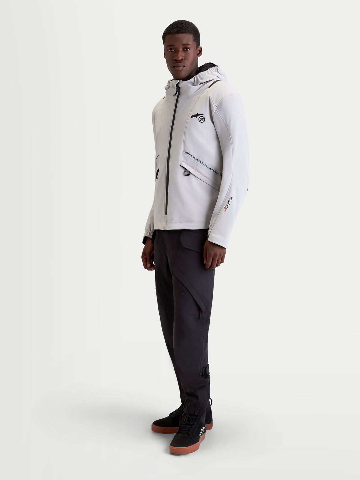 Alpinestars C 5 Drystar Giacca, giacca da moto urbana contemporanea da uomo in grigio chiaro e nero, indossata da un modello che mostra la struttura softshell impermeabile, il cappuccio integrato e le caratteristiche protettive