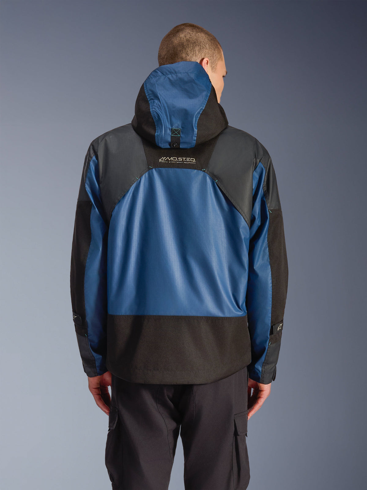 Alpinestars Giacca Mospher Waterproof in Black Dark Petrol, vista posteriore di un parka da moto con pannelli blu in ripstop e sezioni rinforzate nere, branding MO.ST.EQ. sulla parte superiore della schiena, design tattico urbano moderno