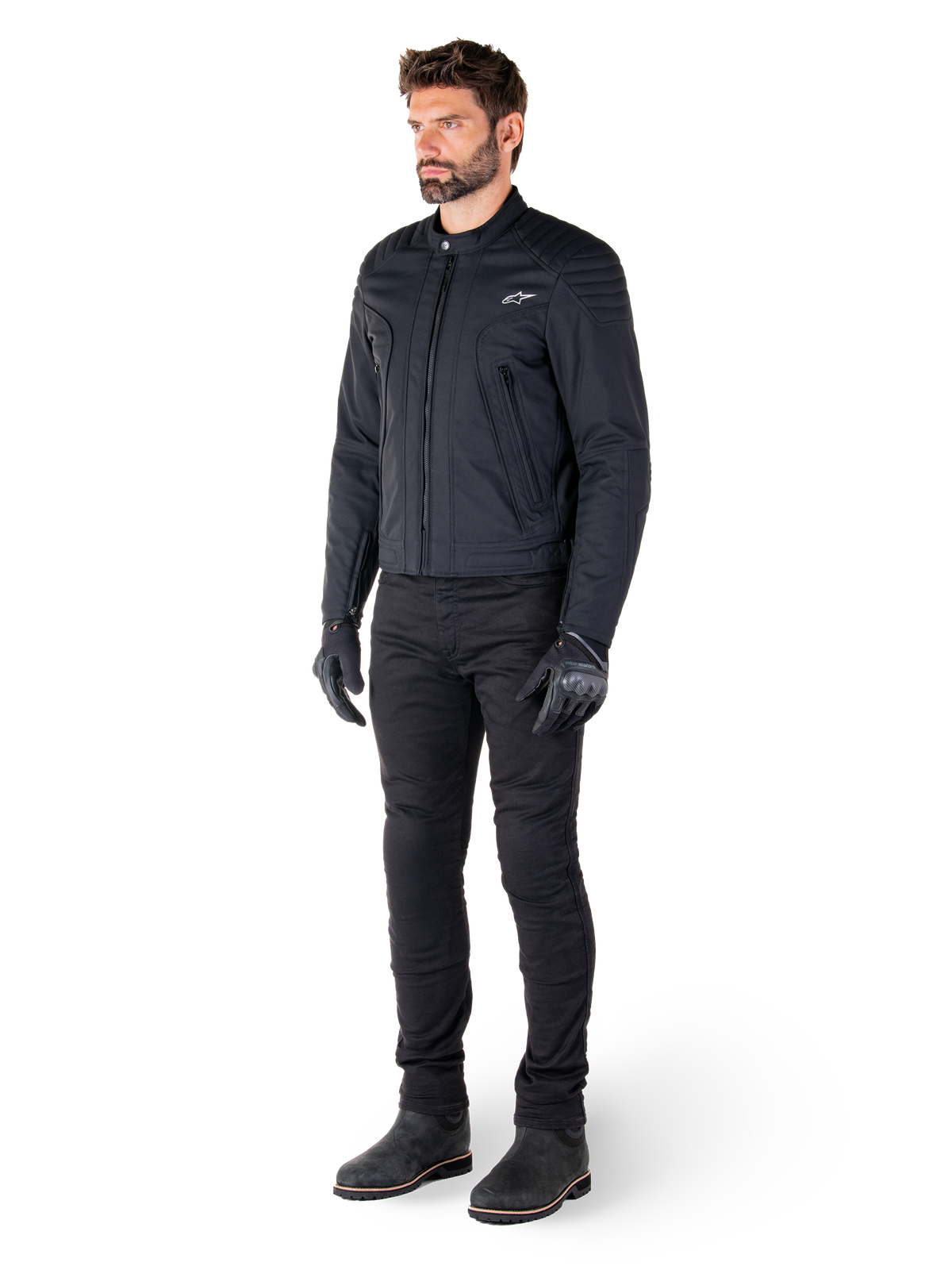 Pilota che indossa la giacca Alpinestars Clayton WR, giacca da moto urban nera, design slim-fit con dettagli trapuntati sulle spalle e finitura opaca, abbinata a pantaloni tecnici da guida e guanti neri.