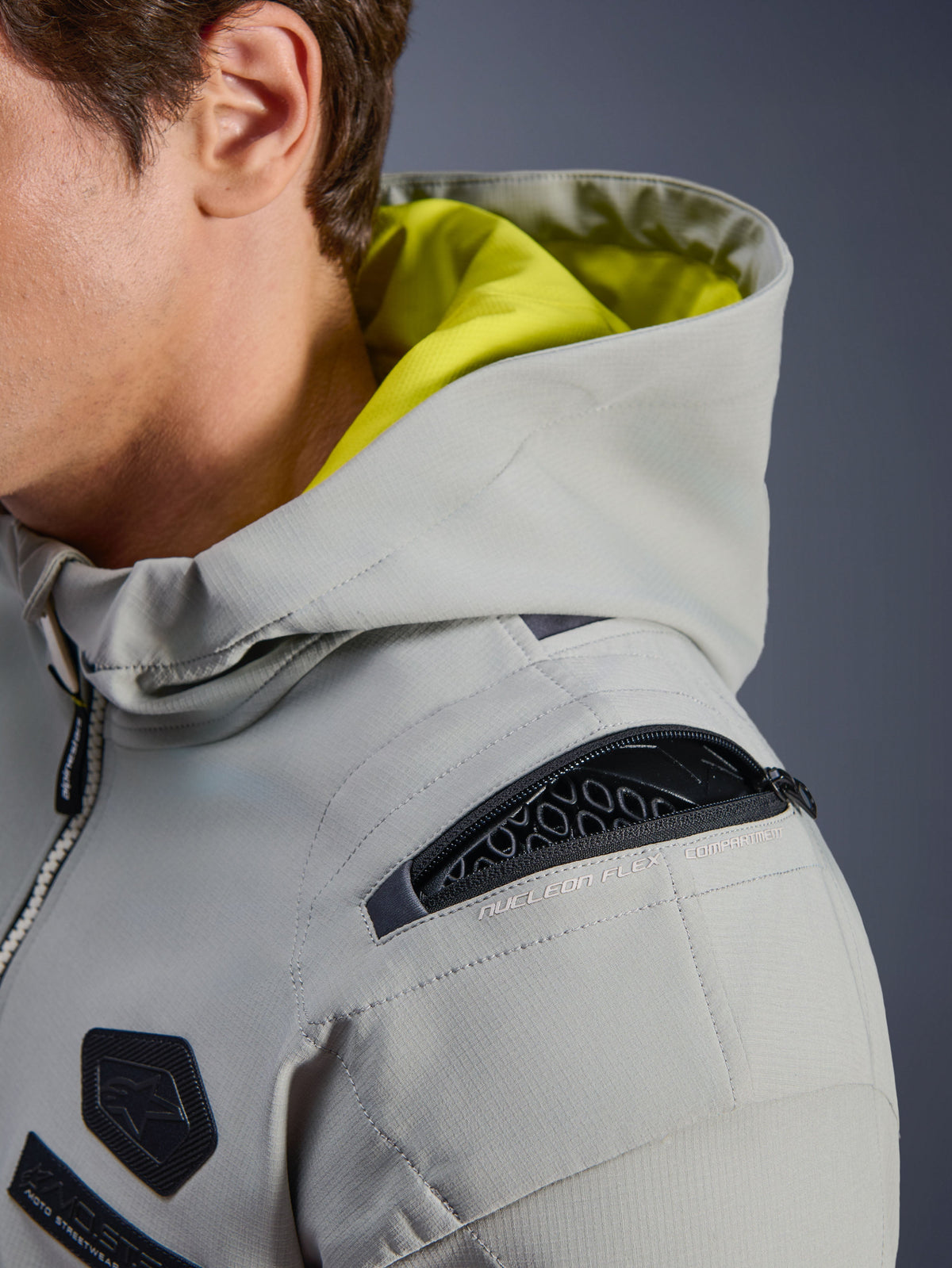Giacca Alpinestars Moblast WP, Iron Gray, primo piano della spalla con scomparto aperto per la protezione Nucleon Flex, interno del cappuccio giallo neon, abbigliamento tecnico da moto urbano con cerniere funzionali