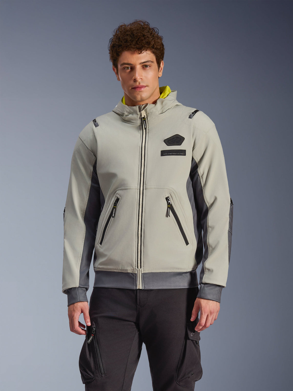 Alpinestars Moblast Waterproof Jacket, felpa con cappuccio da moto urbana grigio chiaro e grigio scuro con fodera gialla, tasche anteriori e cerniere nere, indossata con pantaloni cargo neri, design sportivo moderno