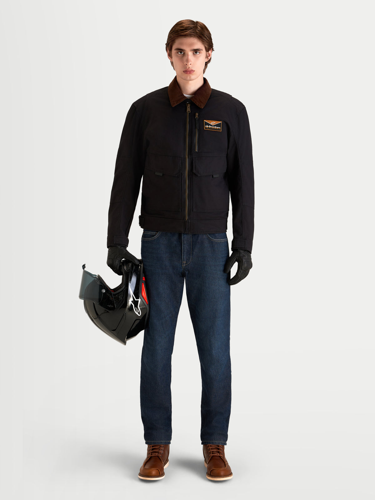 Alpinestars Mustang Wp Giacca, giacca da moto urbana contemporanea da uomo in grigio scuro e marrone scuro, vista frontale su un modello che indossa abbigliamento protettivo e tiene un casco