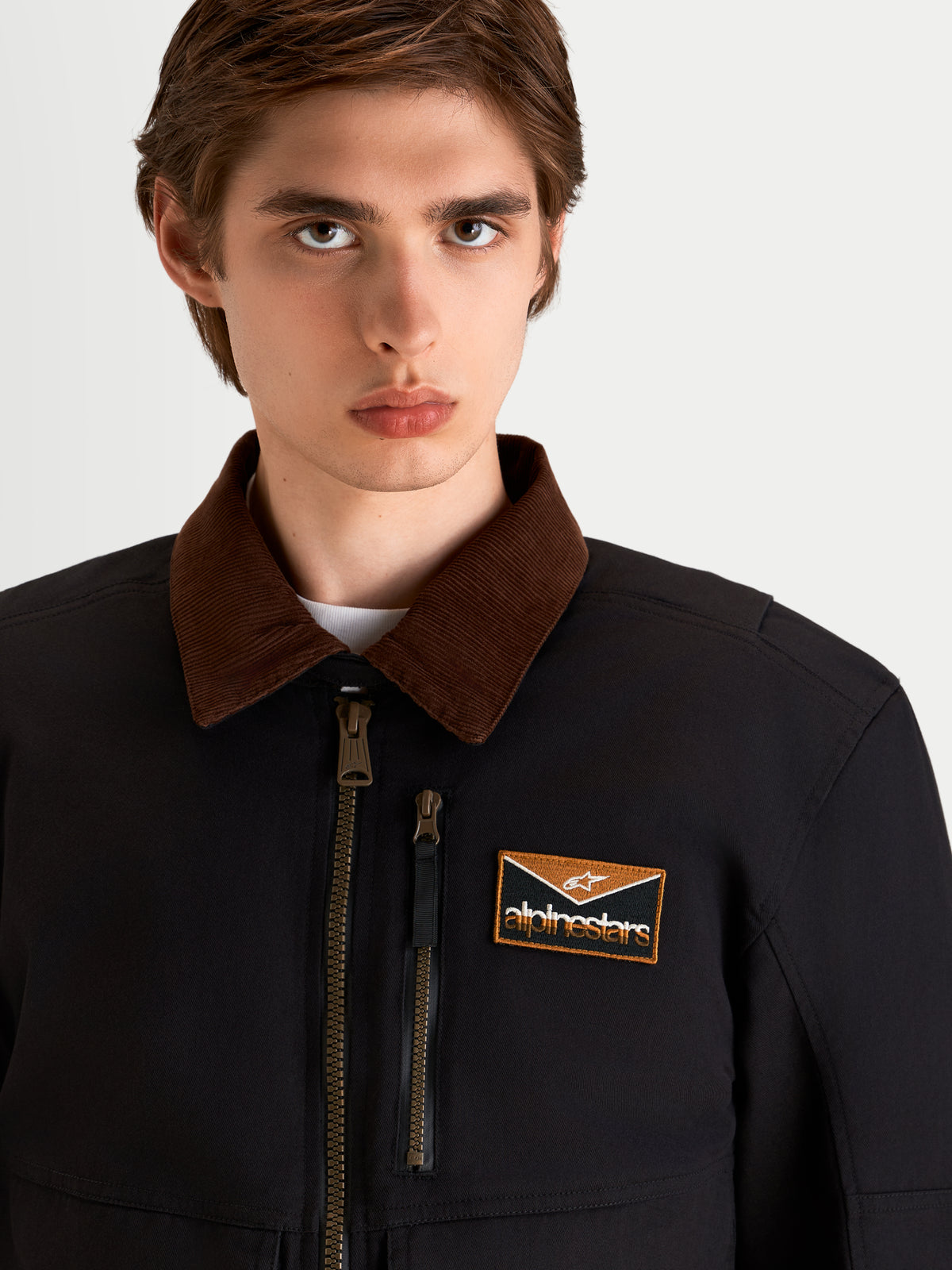 Alpinestars Mustang Wp Giacca, giacca da moto urbana contemporanea da uomo in grigio scuro e marrone, primo piano che mostra il colletto in velluto a coste, la zip frontale e la toppa con logo sul petto indossata da un modello