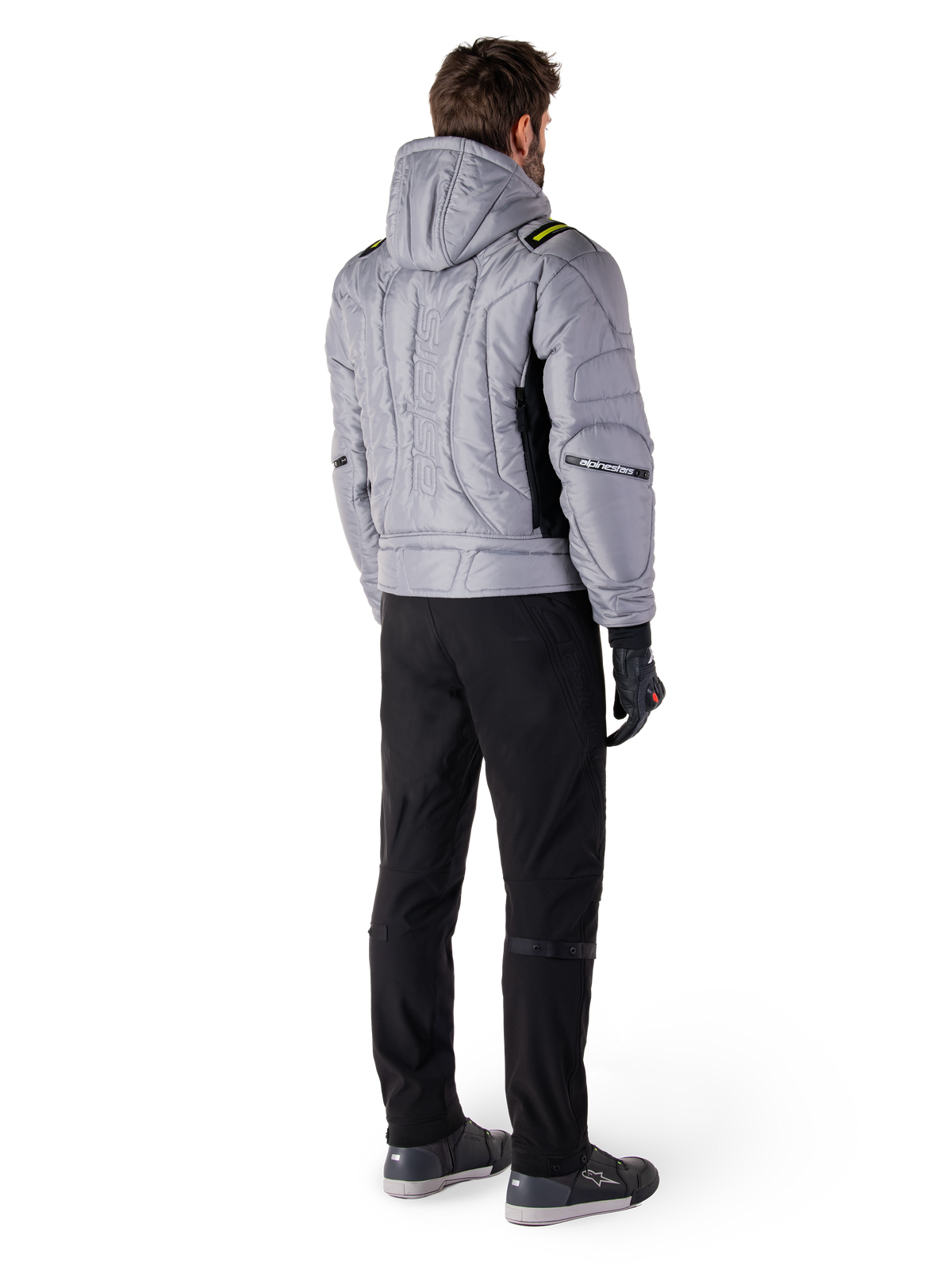 Giacca Alpinestars Mohobbs Waterproof, Lunar Gray Lime Punch, vista posteriore di giacca da moto in stile bomber trapuntata con cappuccio, con scritta Alpinestars sul retro, indossata con pantaloni da guida e guanti neri, streetwear urbano da moto