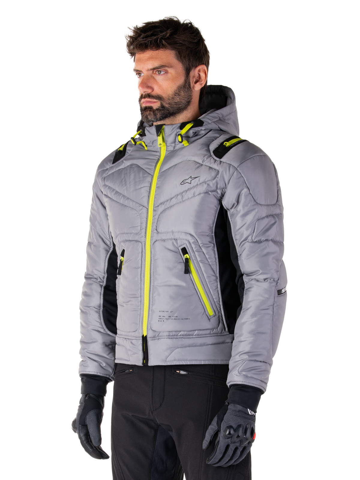Giacca Alpinestars Mohobbs Waterproof, Lunar Gray Lime Punch, giacca da moto bomber trapuntata da uomo con cerniere e dettagli coulisse giallo neon, indossata con pantaloni da guida e guanti neri, design moderno urban moto streetwear con profilo con cappuccio