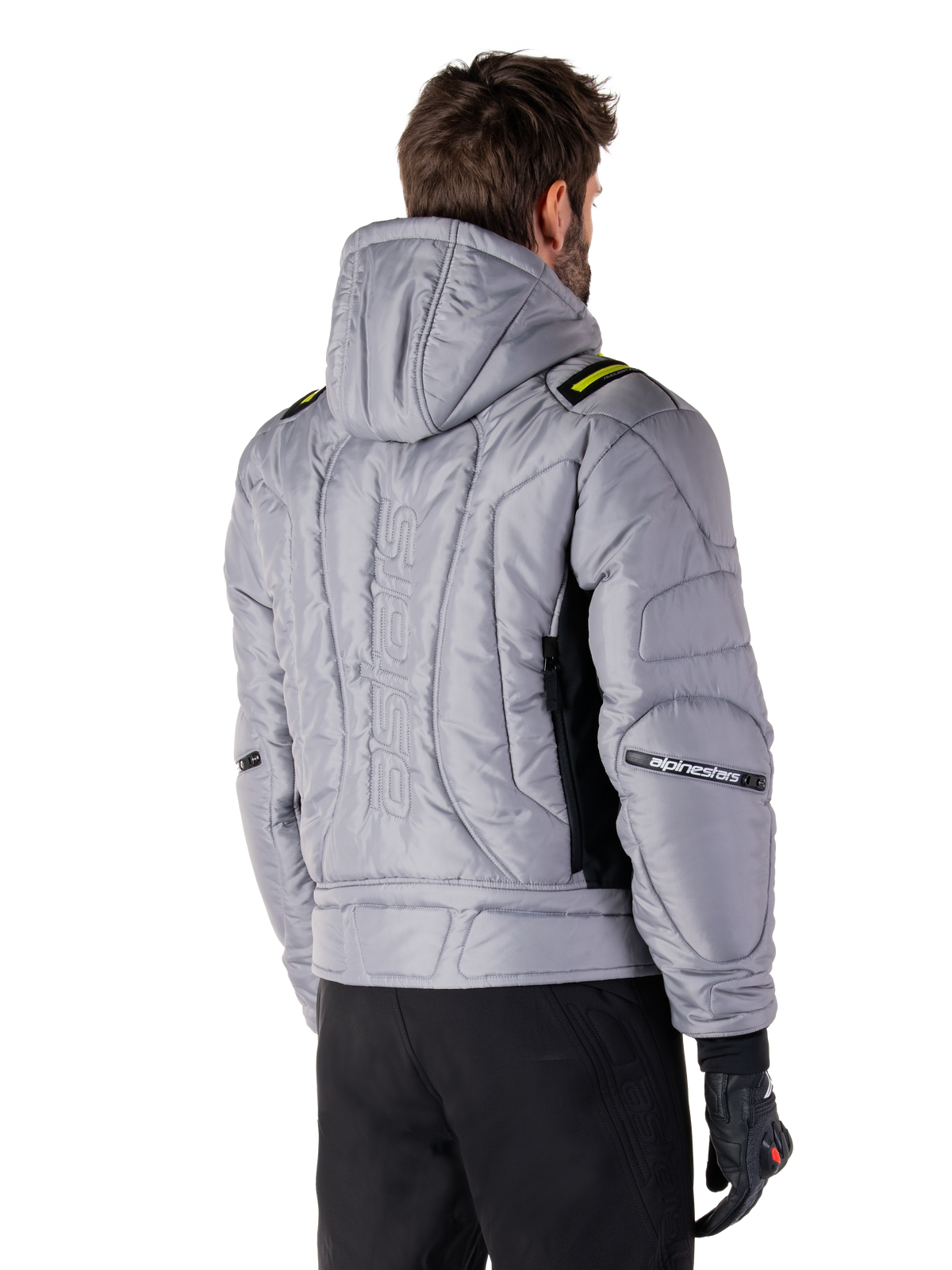 Giacca Alpinestars Mohobbs Waterproof in grigio e verde lime, vista posteriore su un modello, design bomber imbottito e trapuntato con marchio astars goffrato in verticale sul retro, dettagli verde lime sulle spalle, con cappuccio, indossata con pantaloni da moto e guanti neri.