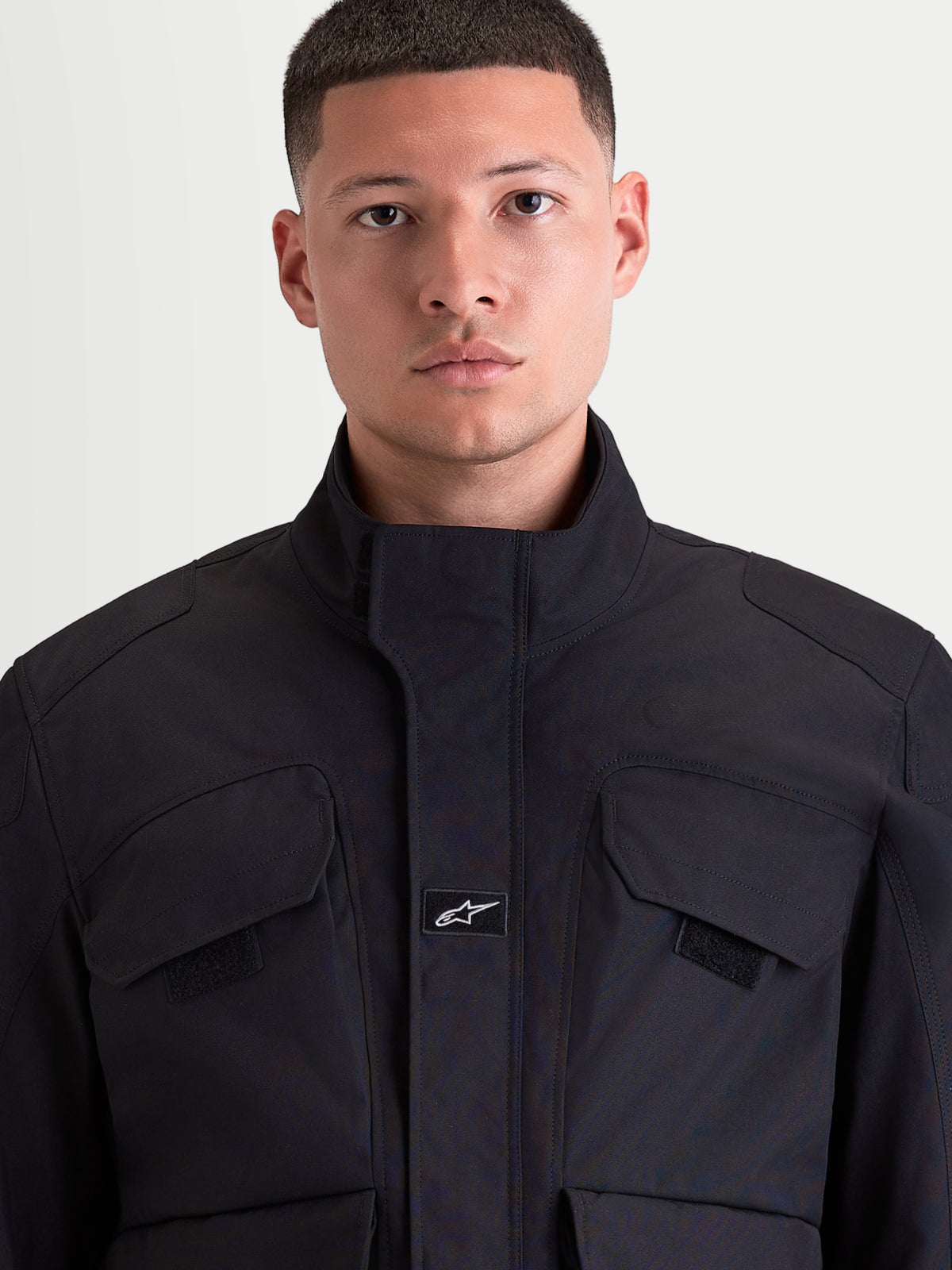 Alpinestars Altan Drystar Giacca, giacca da moto urban contemporary da uomo in colore nero, vista frontale in primo piano che mostra la costruzione in tessuto polyfabric, il colletto caldo integrato e le tasche cargo sul petto indossate da un modello