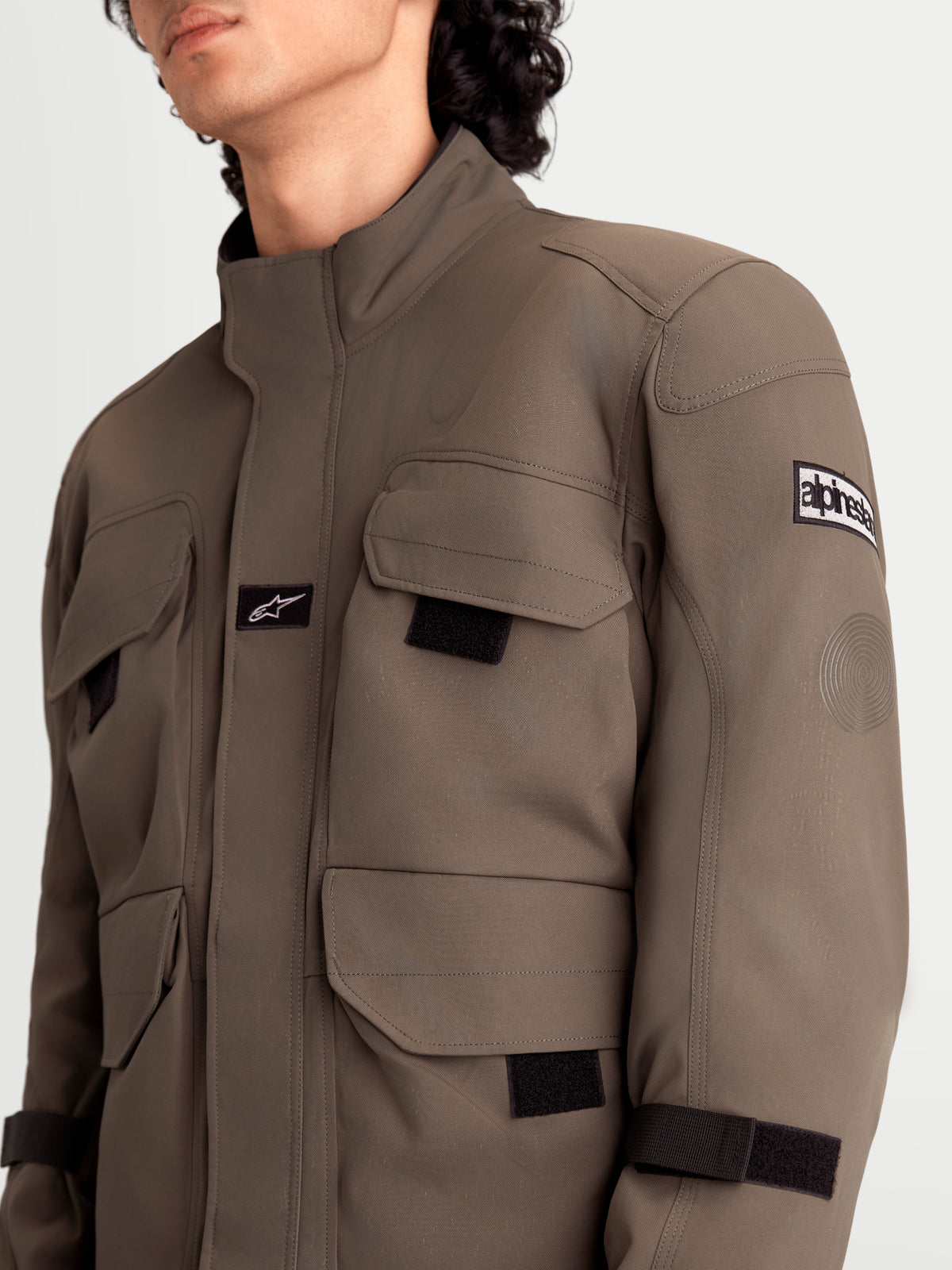 Alpinestars Altan Drystar Giacca, giacca da moto urbana contemporanea da uomo in marrone noce e nero, primo piano con tasche cargo da campo, struttura in tessuto polyfabric e dettaglio delle protezioni sulle spalle indossata da un modello