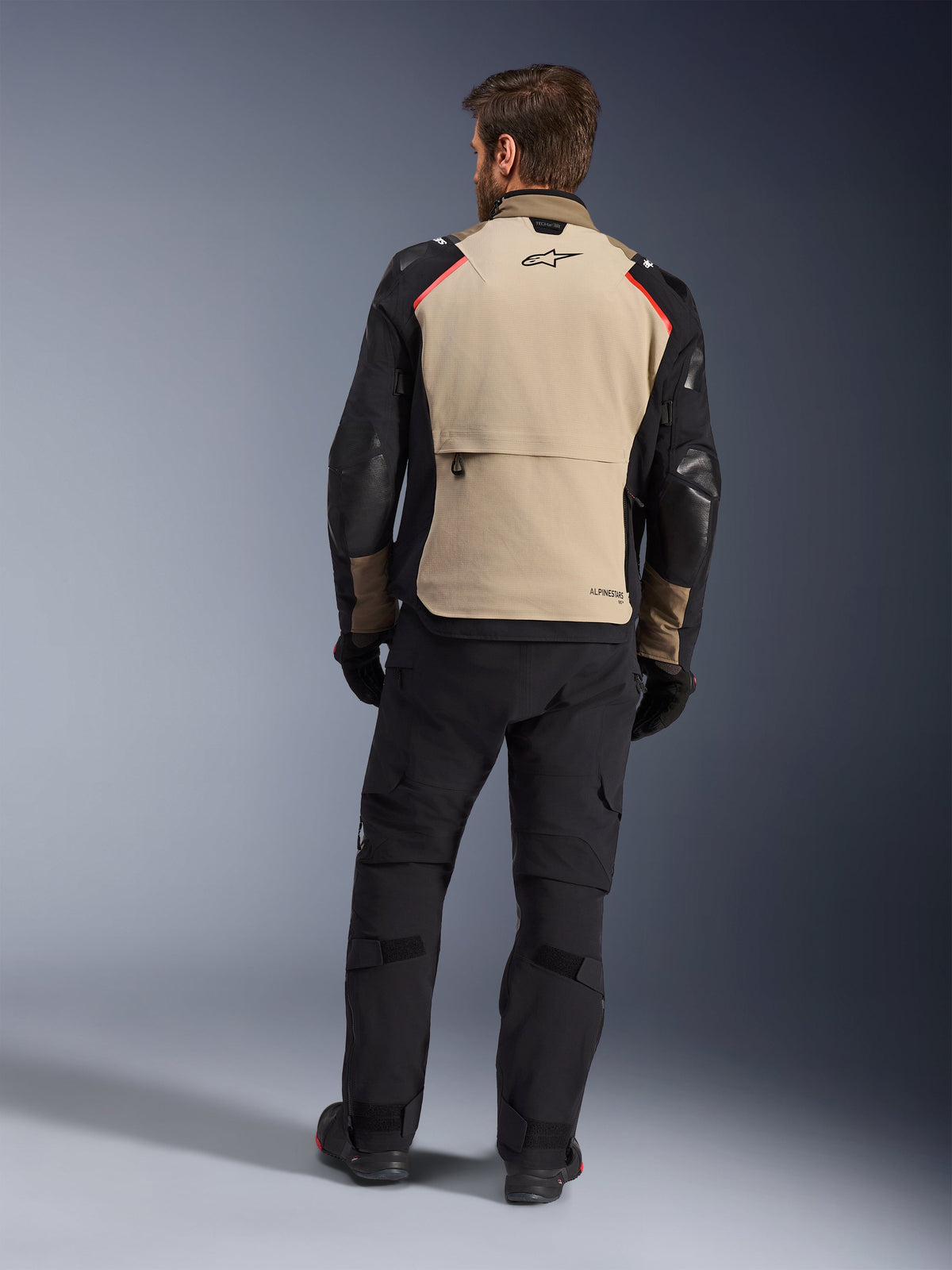 Giacca Alpinestars Andes Pro Drystar® XF, Walnut Aluminum, vista posteriore, giacca da moto adventure con maniche nere e dettagli rossi sulle spalle, indossata con pantaloni da moto e guanti neri