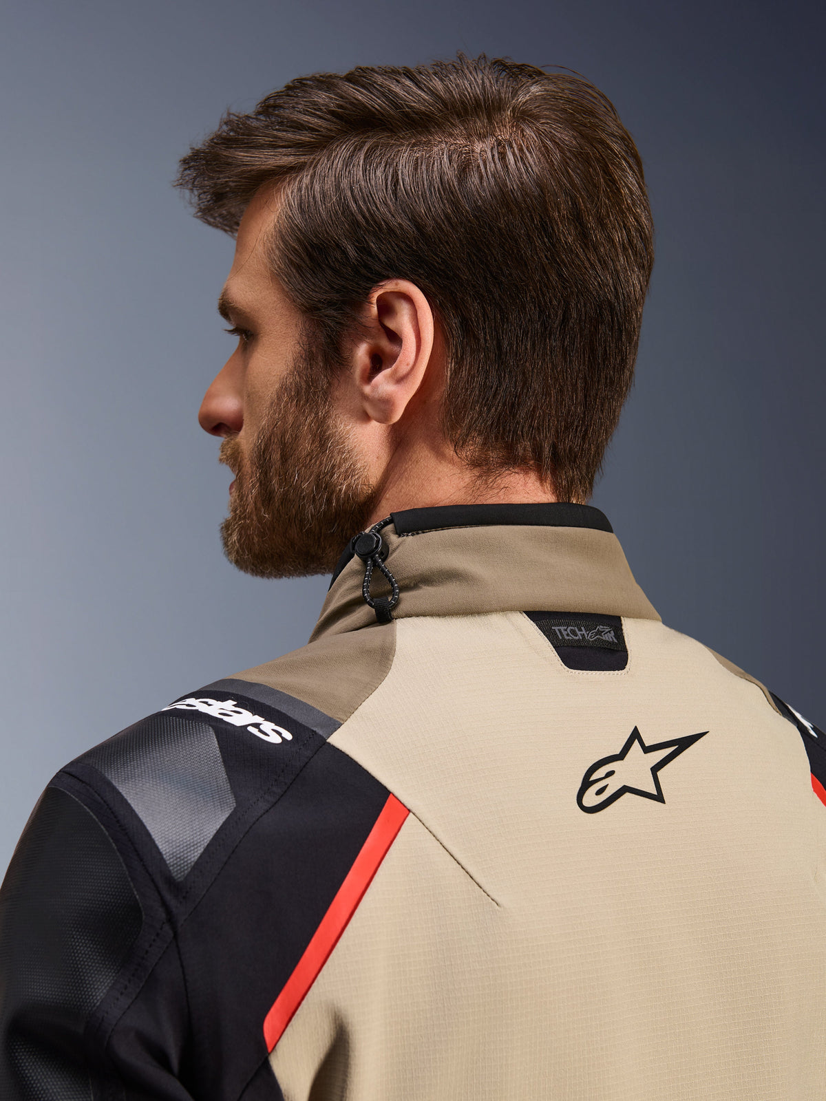 Giacca Alpinestars Andes Pro Drystar® XF in marrone noce e alluminio, vista posteriore ravvicinata di colletto e spalle, con logo Alpinestars, marchio di compatibilità Tech-Air, accenti rossi e sistema di regolazione con cordino elastico sul collo, indossata da un modello
