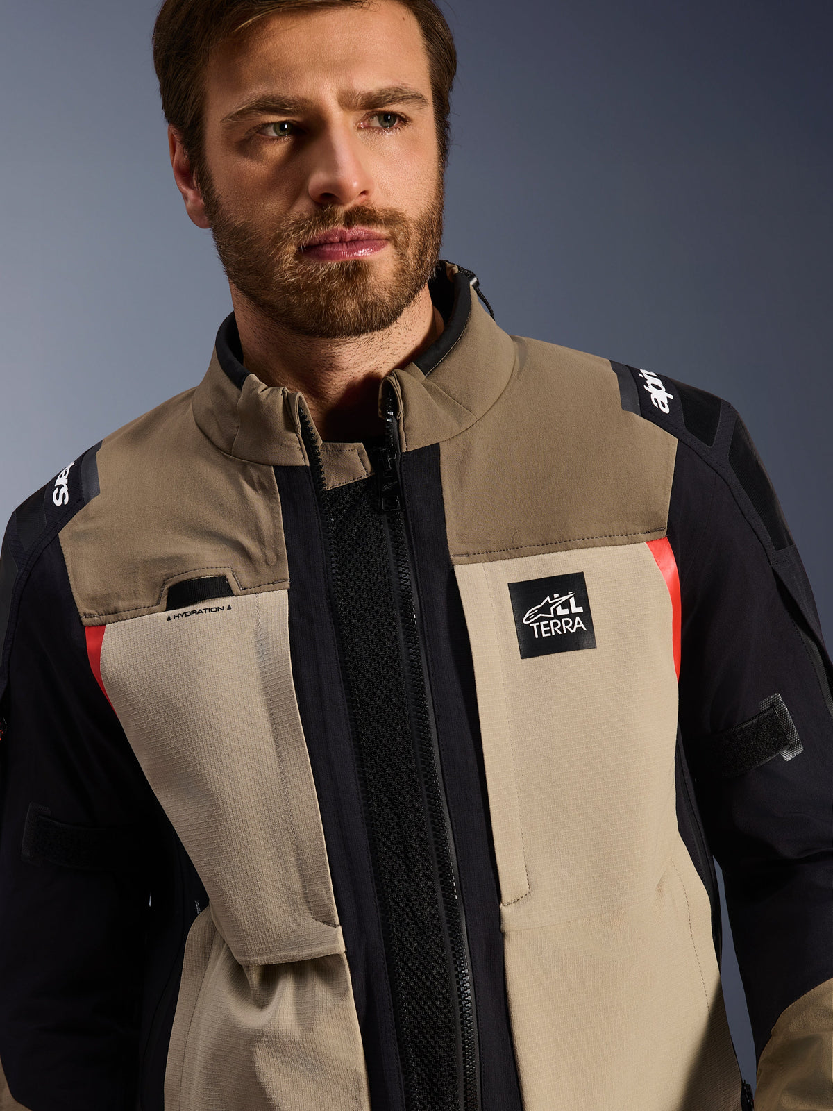 Giacca Alpinestars Andes Pro Drystar® XF in Walnut Aluminum, indossata da un modello, giacca da moto adventure con design tessile a strati in marrone, grigio chiaro e nero con accenti rossi, logo Alpinestars 'TERRA' sul petto e dettagli tecnici visibili.
