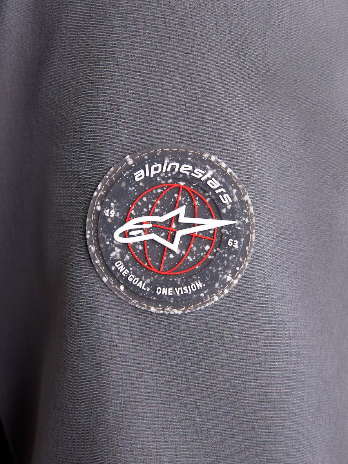 Alpinestars Giacca Therma-Tech WP, dettaglio ravvicinato della toppa circolare con il logo del marchio sulla manica in tessuto grigio scuro e nero, con l'emblema A-star e il marchio distintivo