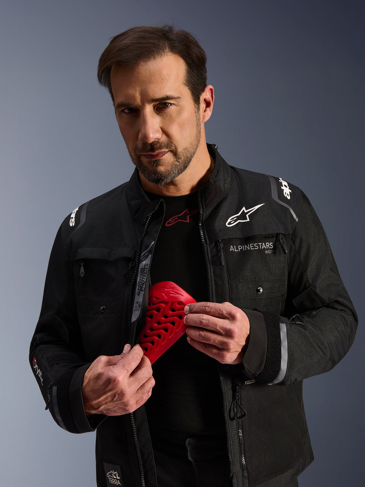 Giacca da moto Alpinestars Cusco Drystar® nera e protezione Nucleon Flex Pro rossa tenuta da un modello uomo.