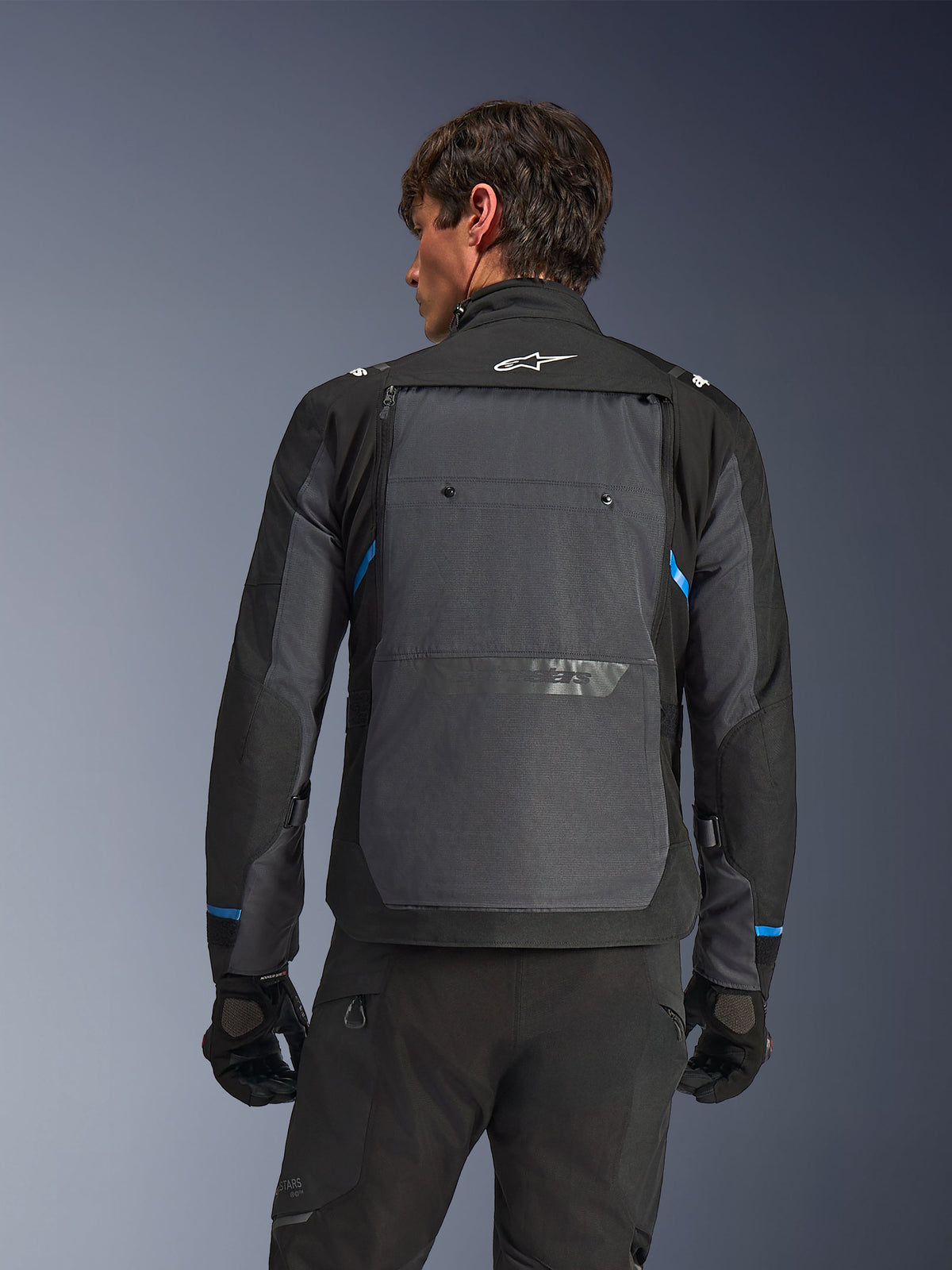 Giacca Alpinestars Cusco Drystar®, giacca da moto, nero e grigio scuro, vista posteriore su un modello con ampio pannello posteriore grigio, logo Alpinestars bianco e accenti blu sulle maniche.