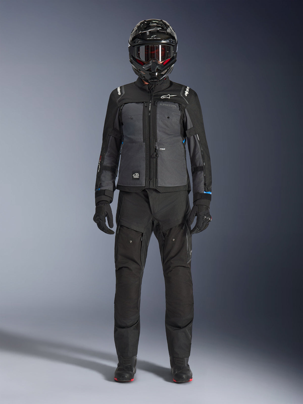 Giacca Alpinestars Cusco Drystar®, giacca da adventure touring in nero e grigio scuro, indossata con pantaloni neri coordinati, guanti e casco integrale, vista frontale a figura intera, abbigliamento protettivo da moto