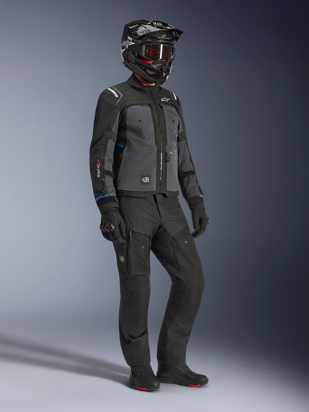 Modello che indossa la giacca Alpinestars Cusco Drystar® in Nero e Deep Gray, abbinata a un equipaggiamento da moto completo con casco nero, pantaloni tecnici coordinati, guanti e stivali, con costruzione in ripstop e softshell per il mototurismo stradale e adventure