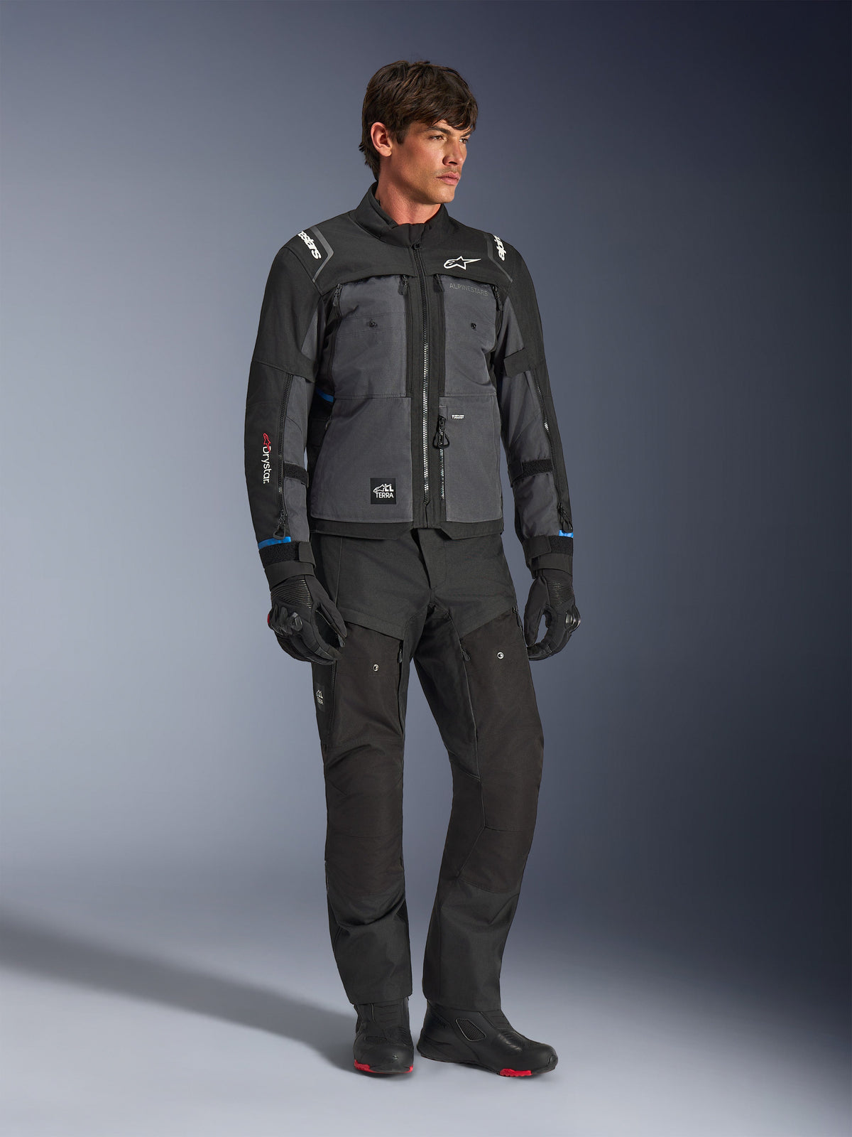 Giacca Alpinestars Cusco Drystar® in nero e grigio scuro, giacca tecnica da moto touring con pannelli multitono, indossata con pantaloni da moto e guanti neri coordinati, progettata per il touring su strada e adventure touring.