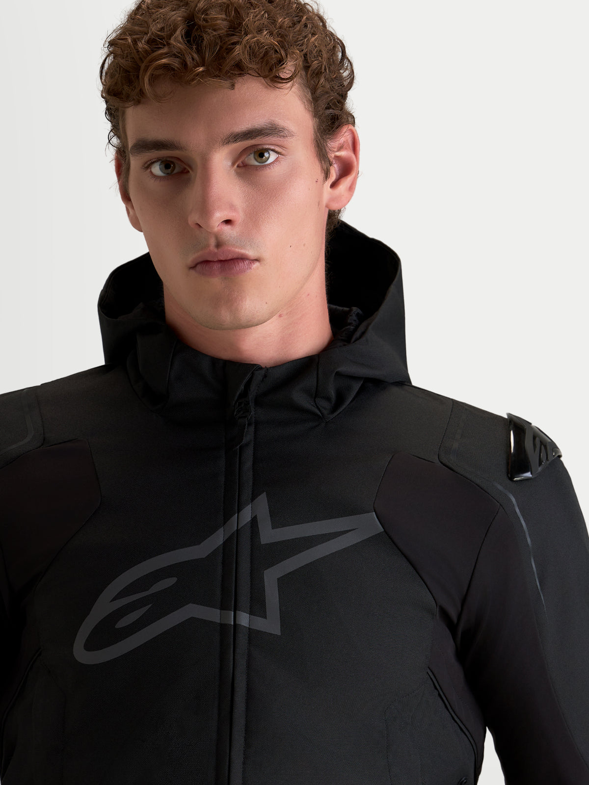 Alpinestars Zaca V 2 Waterproof Giacca, giacca da moto impermeabile da uomo con cappuccio integrato e protezioni spalle DFS, nero, ritratto ravvicinato indossata da un modello