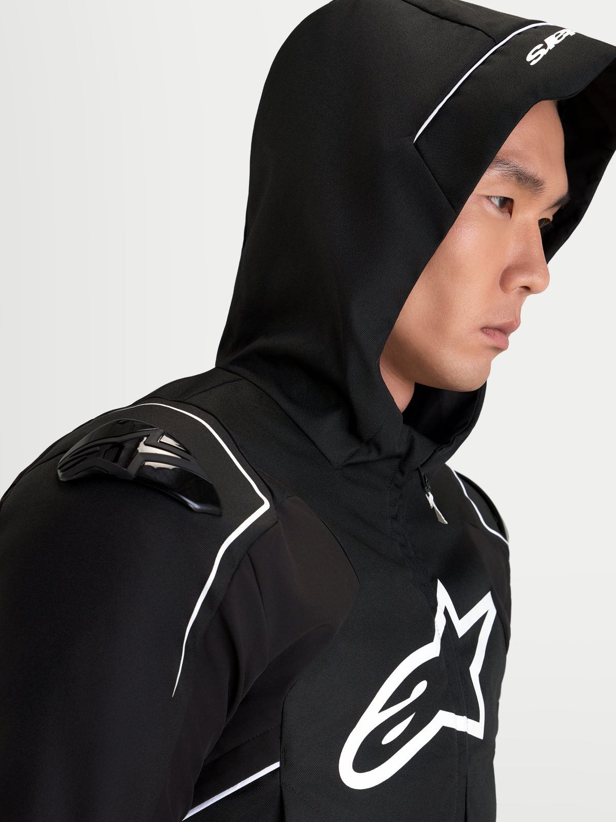 Alpinestars Zaca V2 Waterproof Giacca, giacca sportiva da moto per uomo in nero e bianco, con cappuccio integrato, protezioni spalle DFS e logo Alpinestars sul petto, vista di profilo indossata