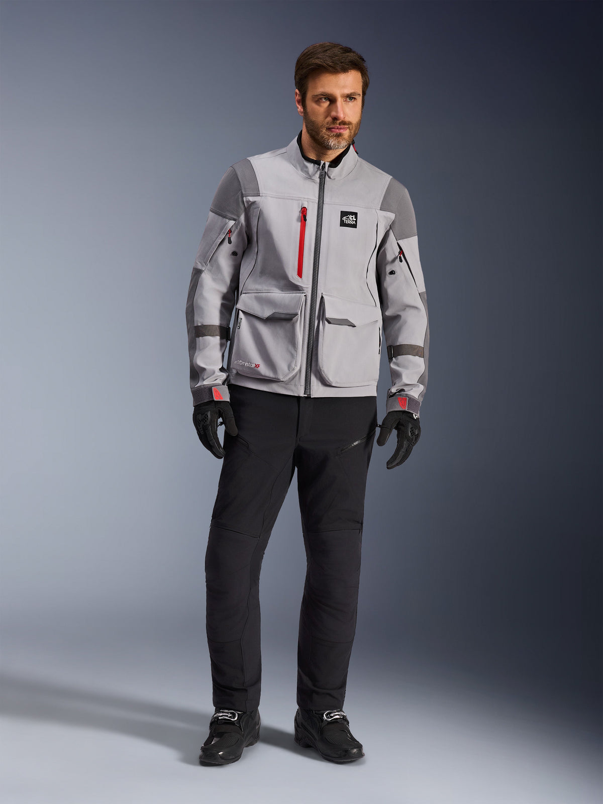 Alpinestars Maxdura Drystar®XF Laminated Armored Shell, giacca da moto adventure, grigio medio e grigio scuro con accenti rossi, indossata con pantaloni e guanti da guida neri, vista frontale che mette in risalto la costruzione tecnica e le grandi tasche cargo.