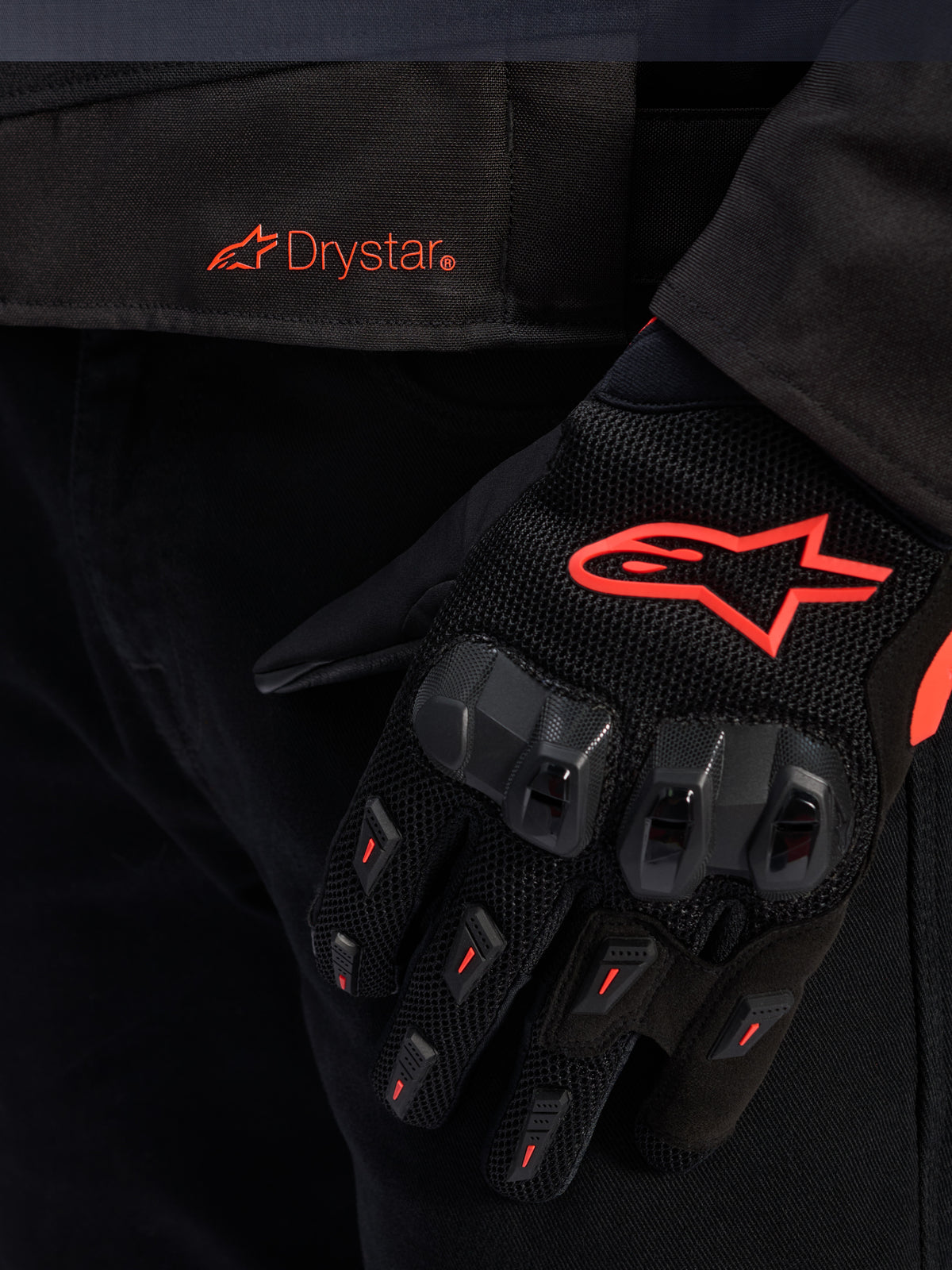 Primo piano della vita della giacca Alpinestars T-GP R V3 Drystar® con logo Drystar rosso, mostrata con guanto da moto nero con logo a stella Alpinestars rosso, tessuto mesh e protezione rinforzata delle nocche.