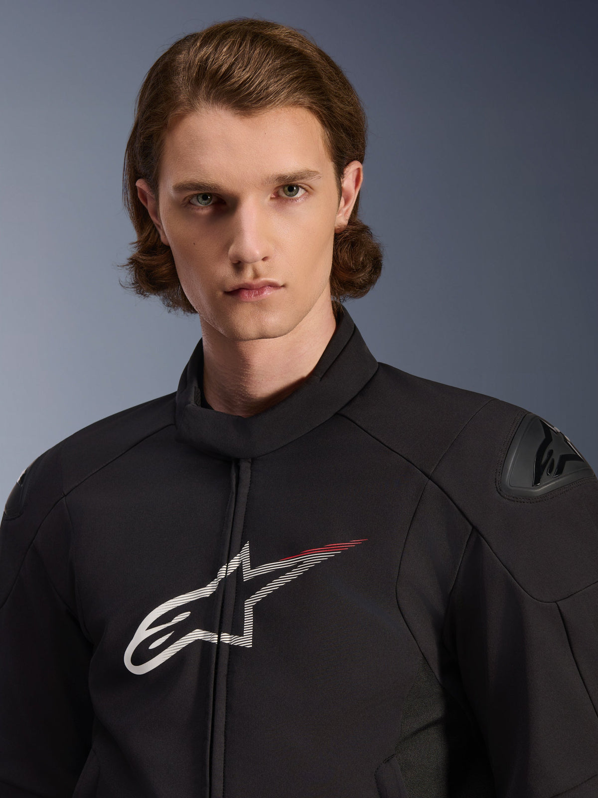 Modello con Giacca Alpinestars SMX Waterproof, nero con accenti bianco e rosso brillante, grande logo a stella bianco con scia rossa sul petto, protezioni per le spalle DFS Lite, struttura in tessuto per prestazioni moto su strada