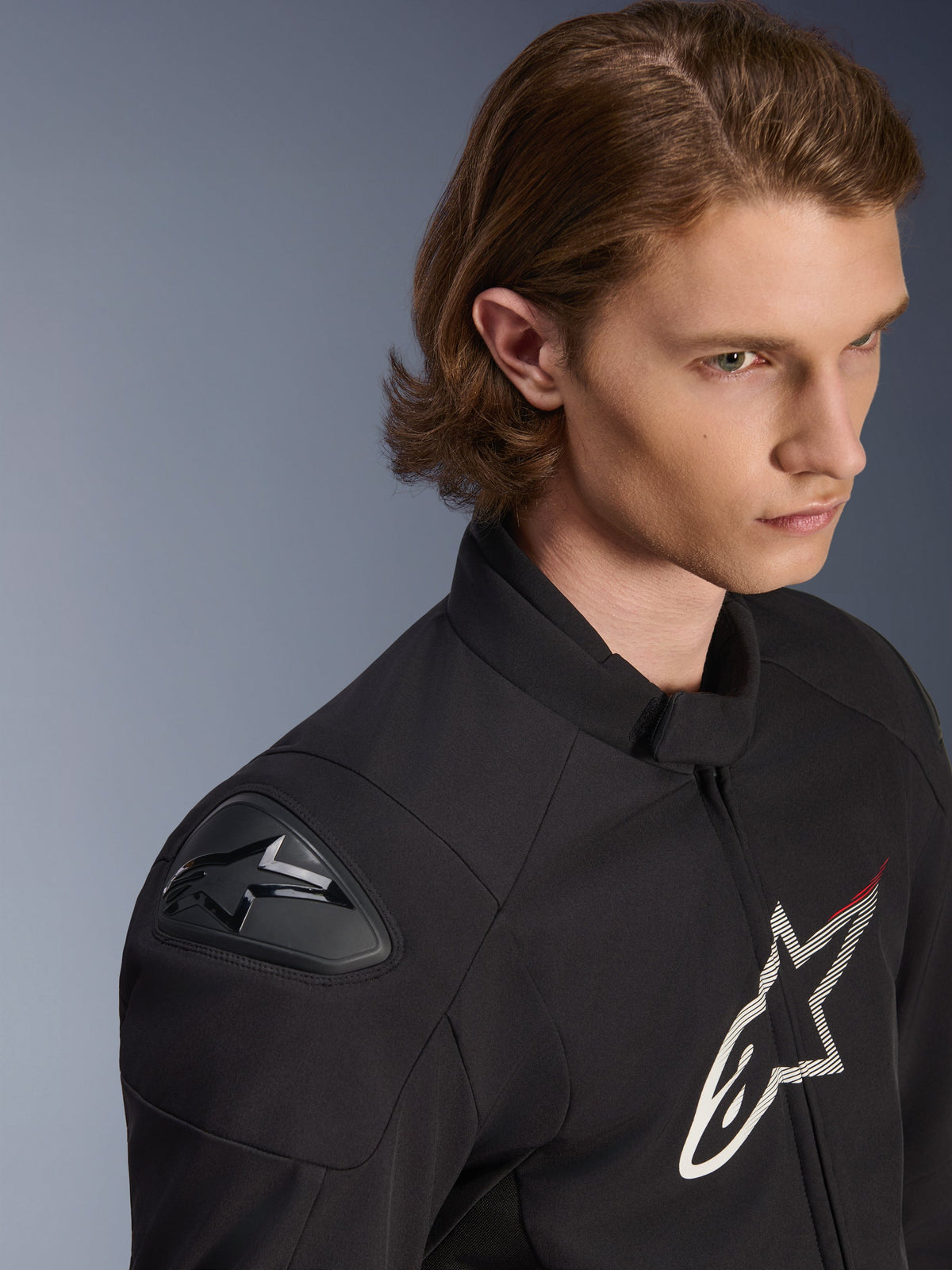 Giacca Alpinestars SMX Waterproof, nero con dettagli bianchi e rossi, primo piano lifestyle su un modello maschile, dotata di slider esterni per le spalle DFS Lite e grande logo a stella sul petto, abbigliamento sportivo da moto