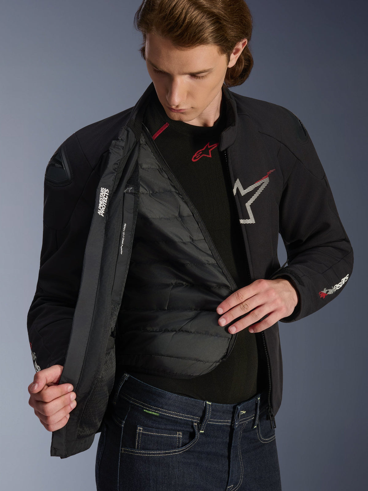 Giacca Alpinestars SMX Waterproof in nero, bianco e rosso brillante, indossata da un uomo e aperta per mostrare la fodera termica trapuntata staccabile, spalle esterne DFS lite, dettagli del logo bianchi, abbigliamento tecnico da moto da strada