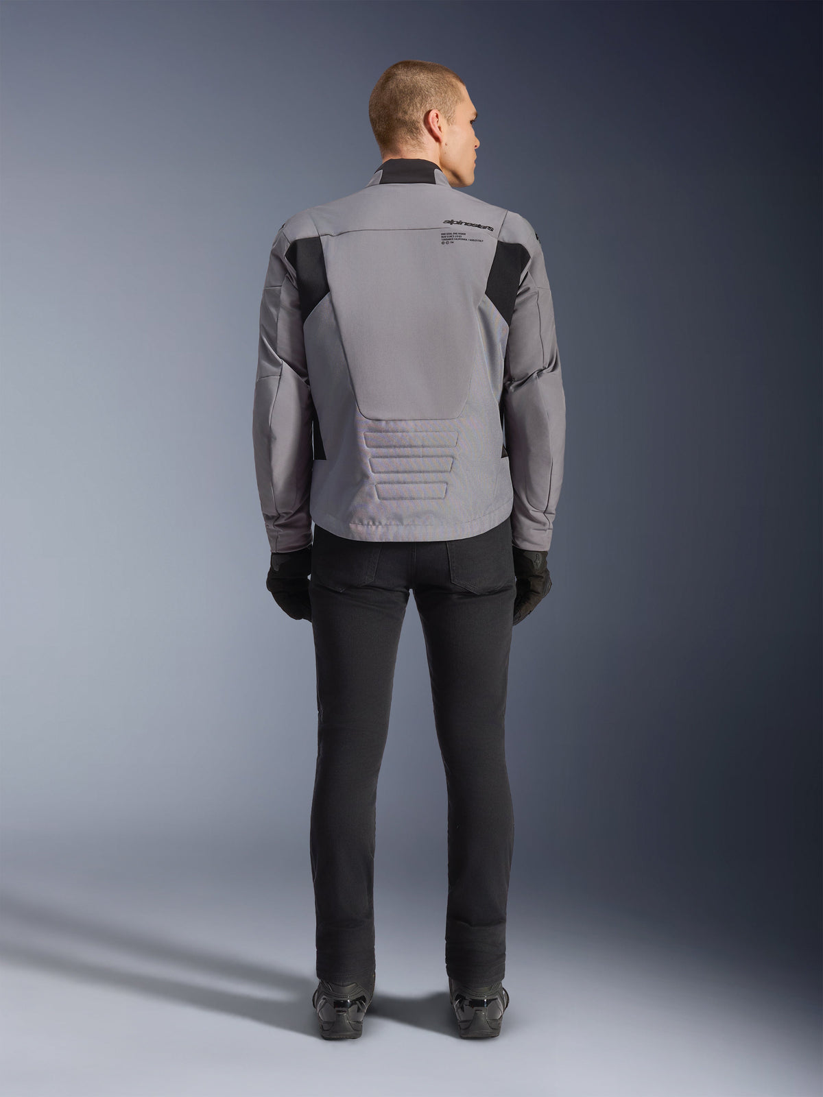 Giacca Alpinestars SMX Waterproof, vista posteriore, grigio scuro e nero, con pannelli in tessuto nero sulle spalle e design con vestibilità sportiva, abbinata a pantaloni e guanti neri per un look completo da motociclismo