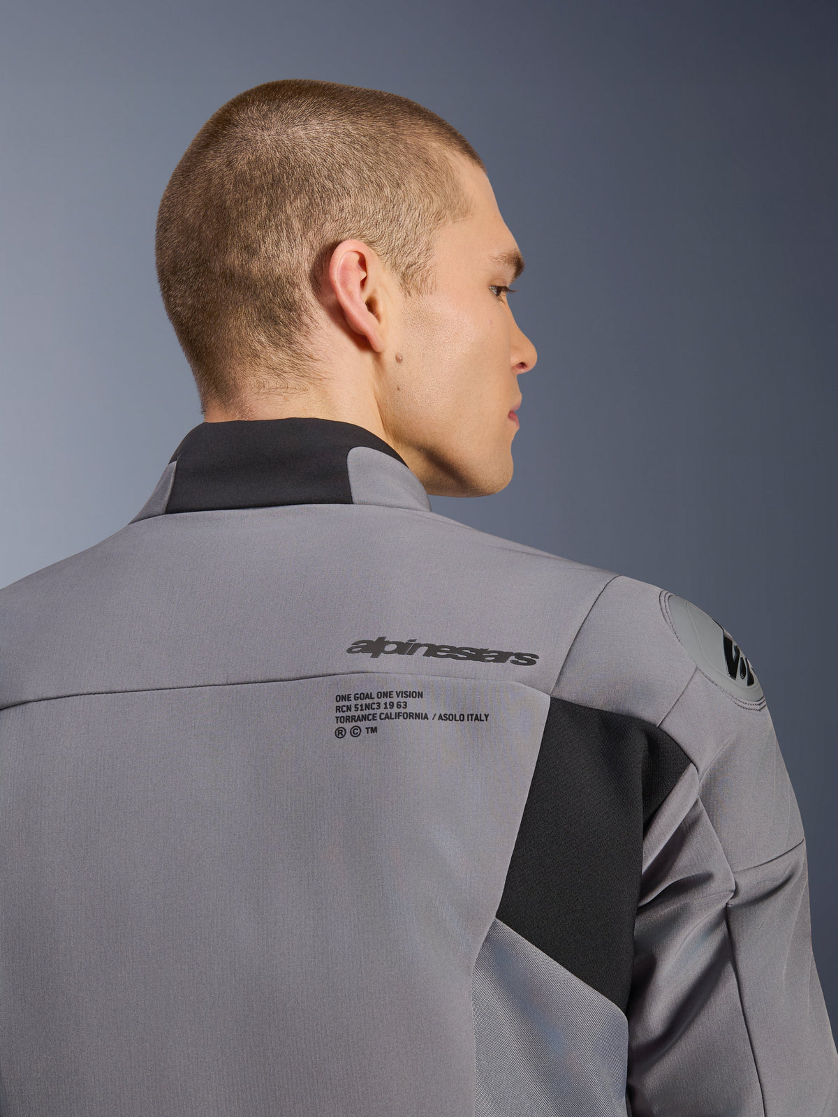 Giacca impermeabile Alpinestars SMX in Dark Gray Black, primo piano della schiena e della zona della spalla che mostra il marchio Alpinestars e la protezione per le spalle DFS lite, indossata da un modello uomo