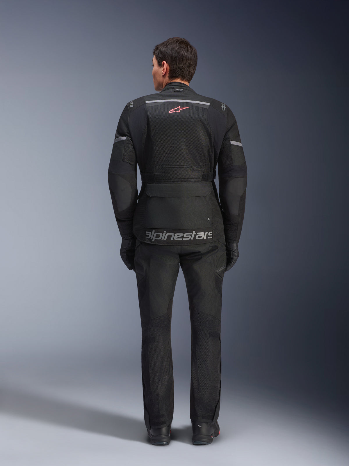 Giacca e pantaloni Alpinestars Andes Air Drystar®, completo da moto touring nero, vista posteriore del pilota, con pannelli in rete, logo a stella rossa e marchio Alpinestars riflettente sulla giacca, indossato con guanti e stivali neri.