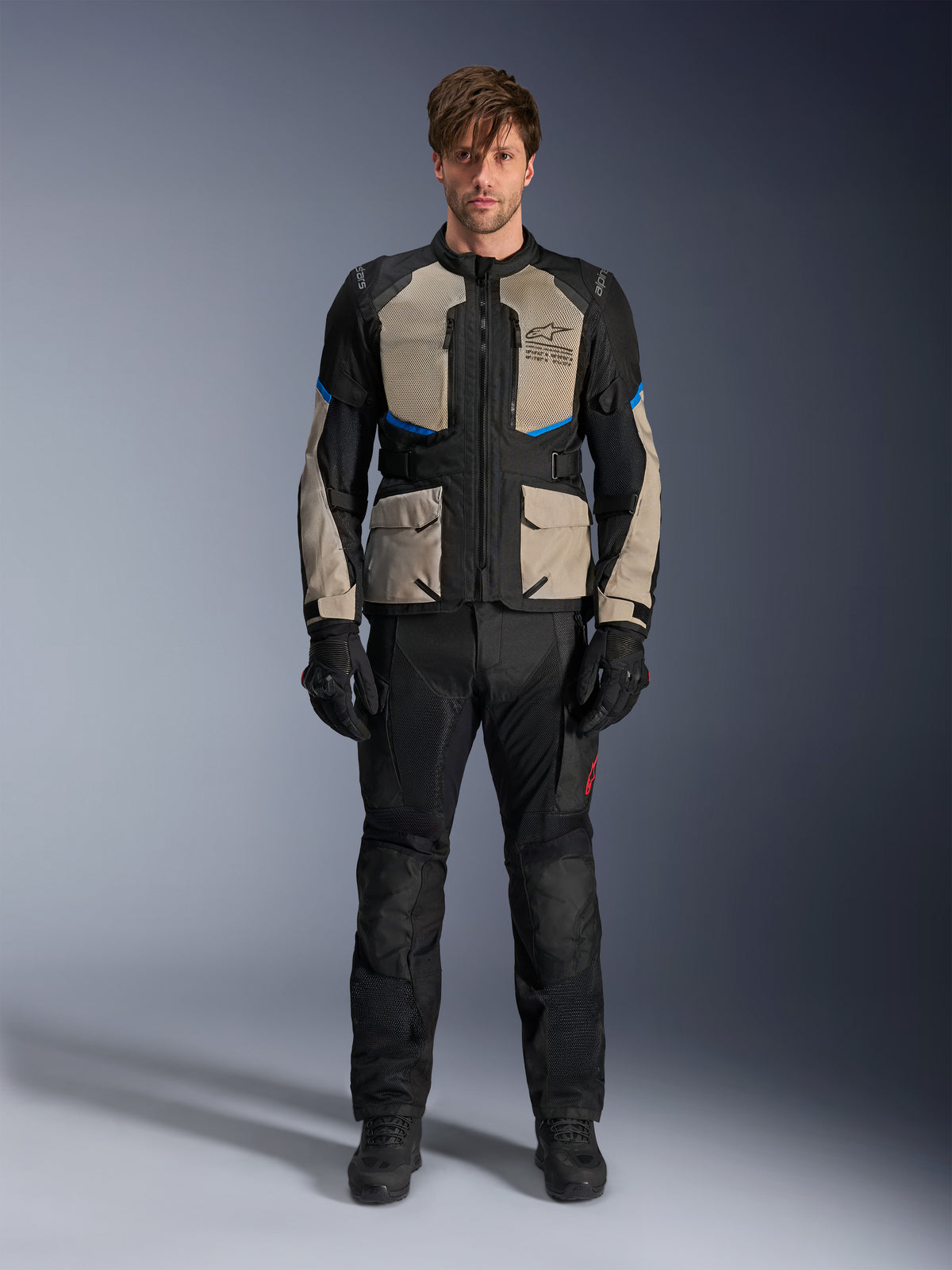 Modello che indossa la giacca Alpinestars Andes Air Drystar®, giacca da moto touring, colore Black Laurel Gray e Bright Blue, abbinata a pantaloni e guanti da guida neri coordinati, con ampi pannelli di ventilazione in mesh su petto e maniche per l'adventure touring in climi caldi.