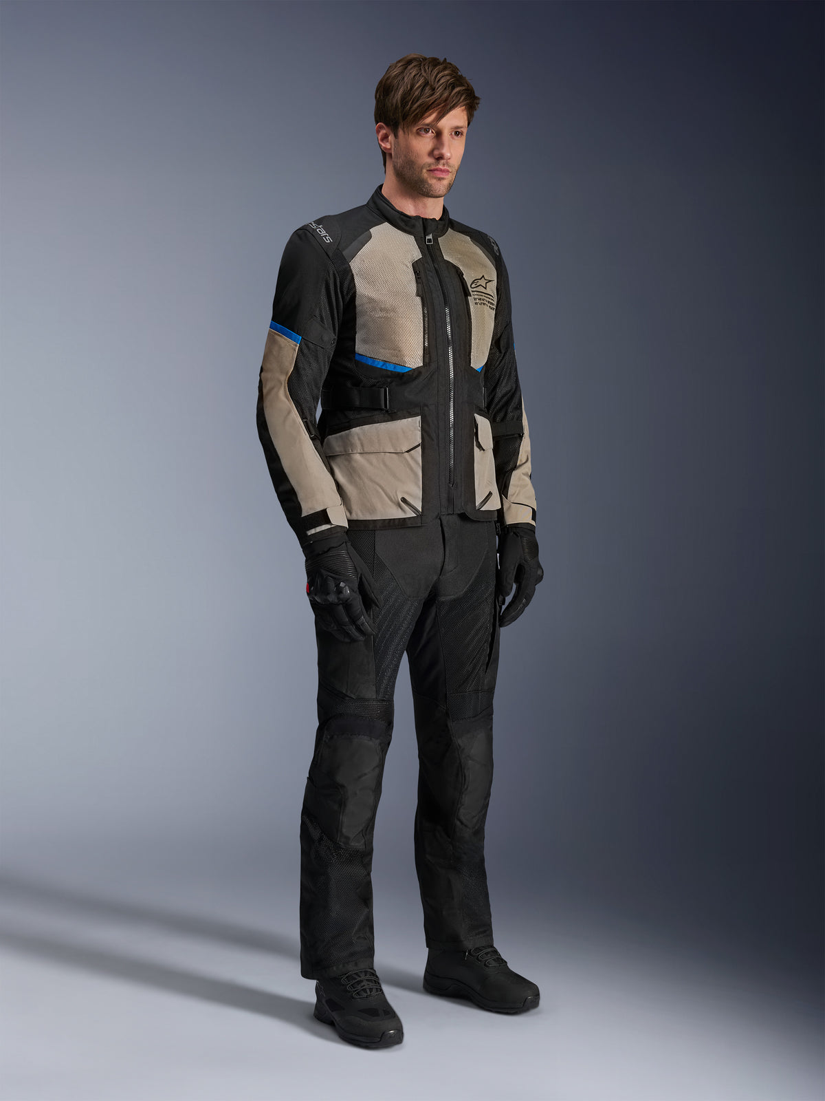 Giacca Alpinestars Andes Air Drystar®, giacca da moto touring, nero, grigio alloro e blu brillante, indossata con pantaloni e guanti da guida coordinati, dotata di ampi pannelli in rete per il flusso d'aria e vestibilità orientata alla strada, equipaggiamento adventure touring