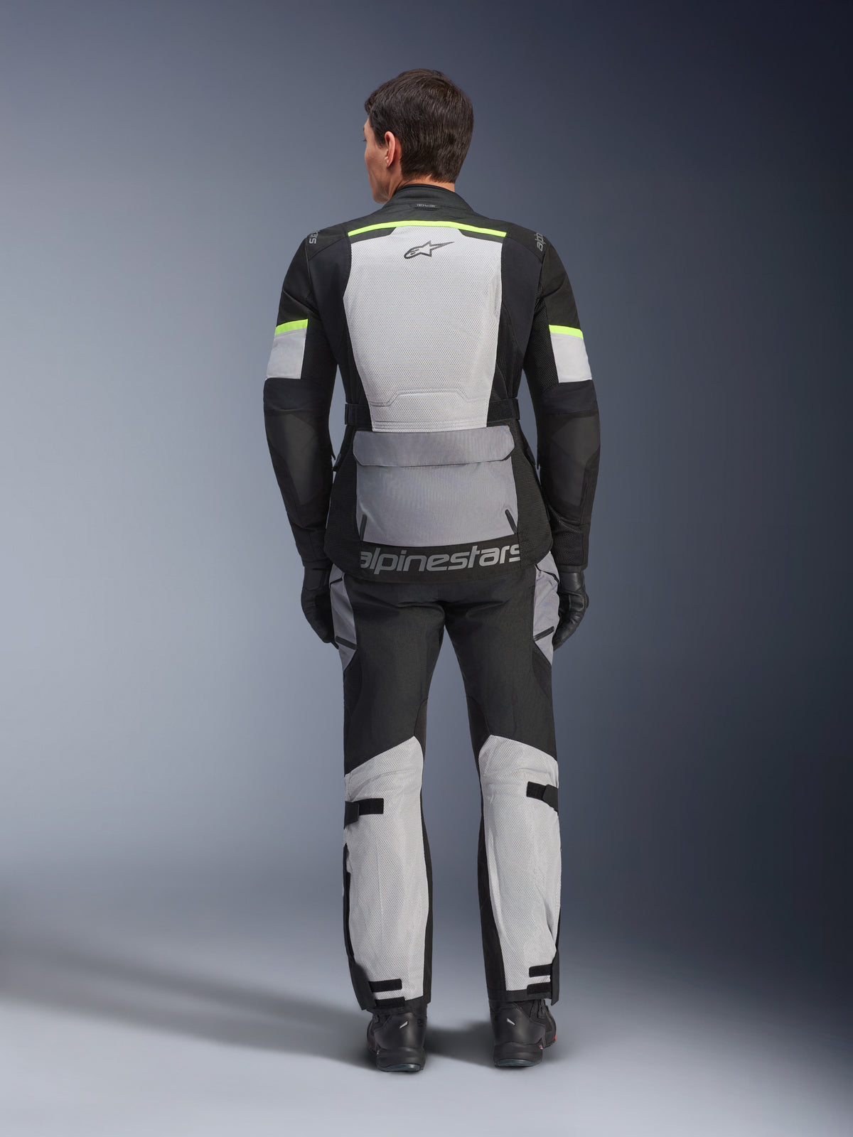 Giacca Alpinestars Andes Air Drystar®, giacca da touring per moto, grigio ghiaccio, grigio scuro e nero, vista posteriore con ampi pannelli in mesh per la ventilazione, dettagli giallo fluorescente e marchio Alpinestars, indossata con pantaloni da touring coordinati
