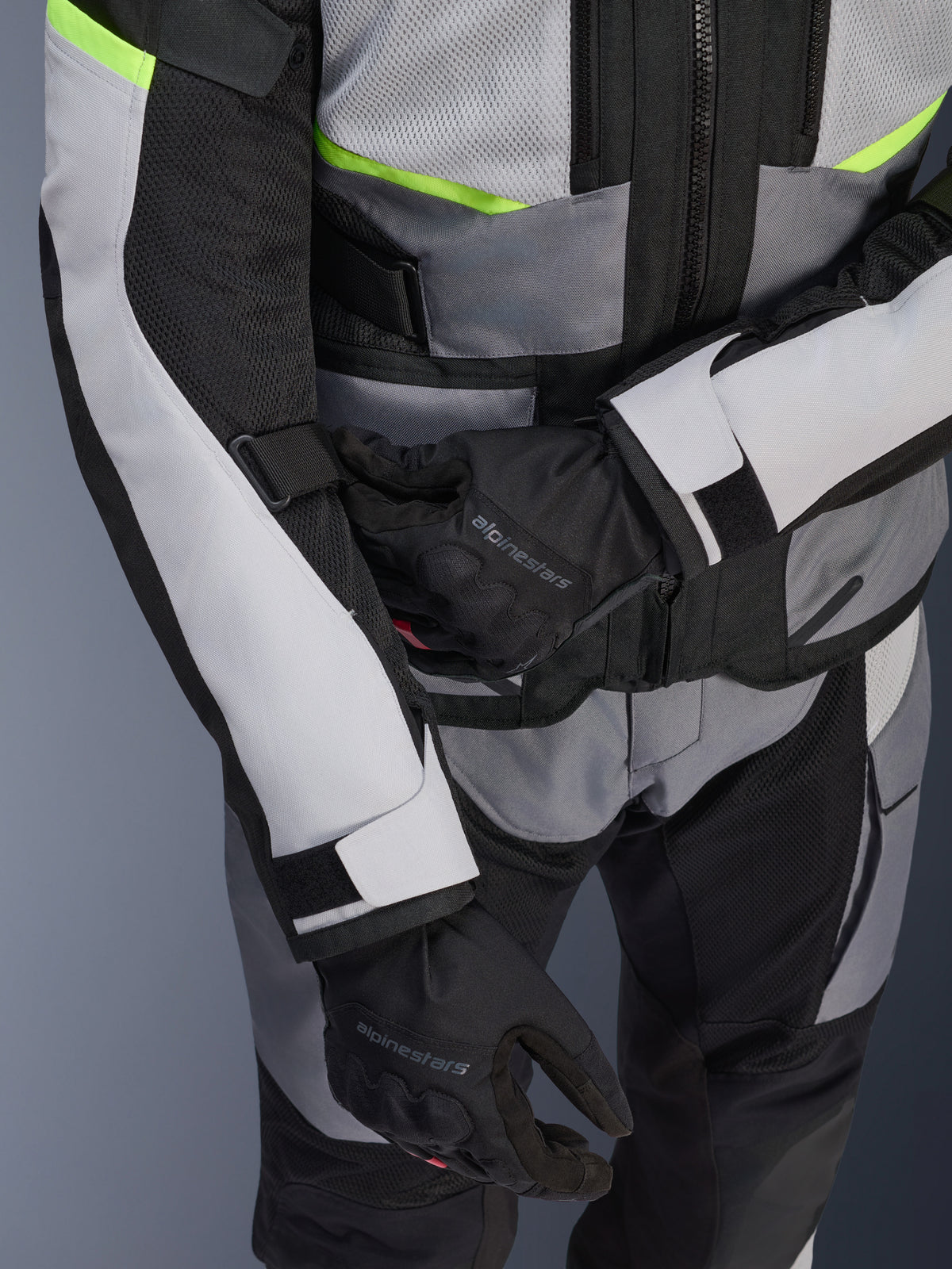 Giacca Alpinestars Andes Air Drystar®, giacca da mototurismo, grigio ghiaccio e grigio scuro con dettagli giallo neon, primo piano che mostra i pannelli in rete e le cinghie di regolazione, indossata con guanti Alpinestars neri