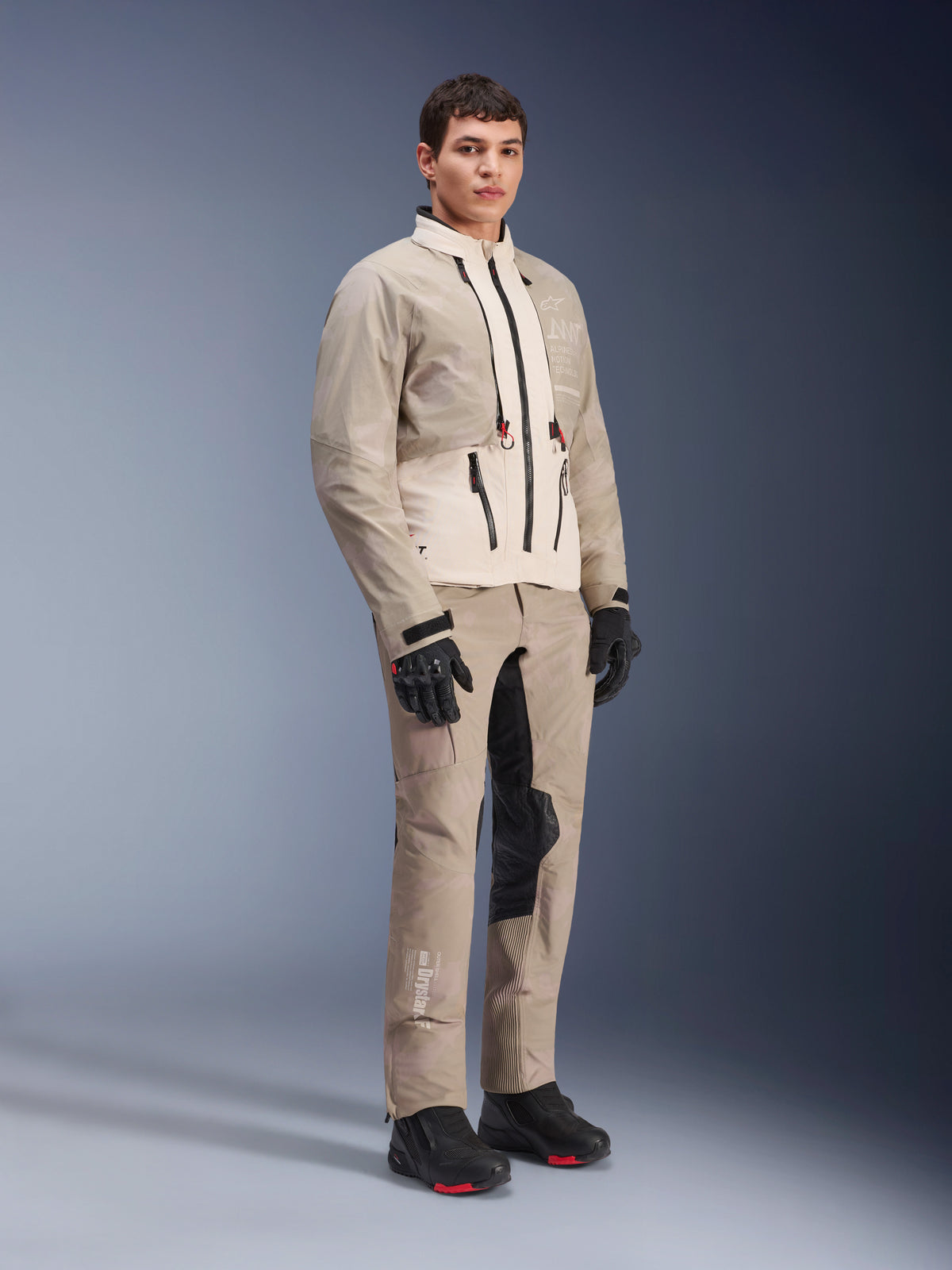Giacca Alpinestars AMT-10LAB Drystar® XF, giacca da moto adventure, White Sand Aluminum Camo, indossata con pantaloni adventure coordinati, guanti e stivali da moto neri, inquadratura a figura intera in studio, abbigliamento protettivo multi-stagione