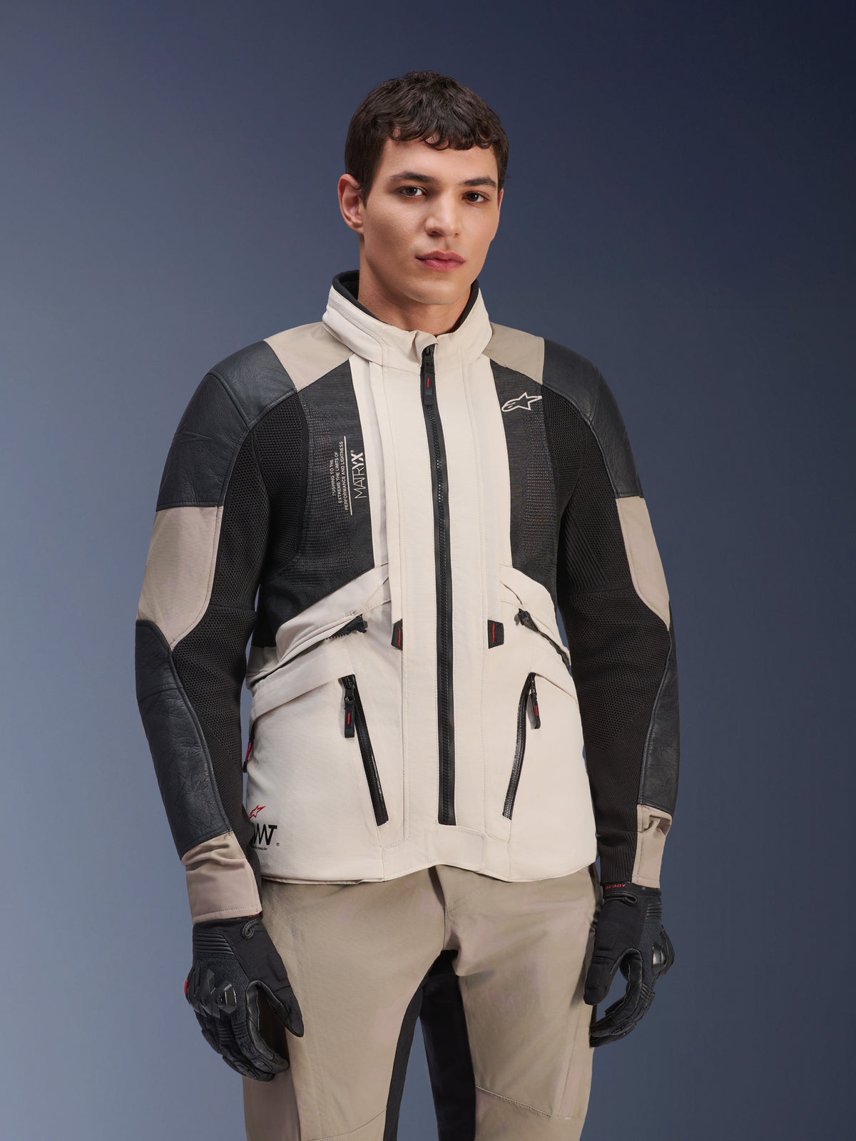 Giacca Alpinestars AMT-10LAB Drystar® XF, White Sand Aluminum Camo, giacca da moto adventure con pannelli in mesh MATRYX® neri e rinforzi in pelle, indossata da un modello con guanti neri e pantaloni coordinati color sabbia, ritratto in studio