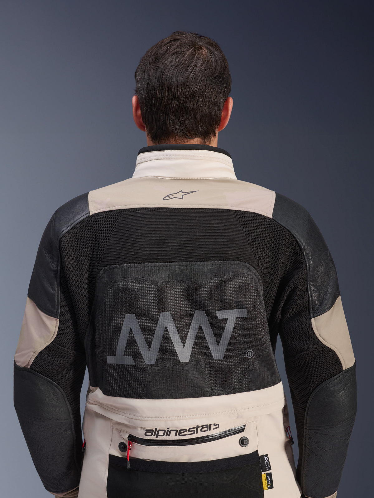 Vista posteriore della giacca Alpinestars AMT-10LAB Drystar® XF in White Sand e nero, con un grande logo AMT sul pannello posteriore in rete, marchio Alpinestars sulla parte bassa della schiena e costruzione in tessuto tecnico per il motociclismo adventure