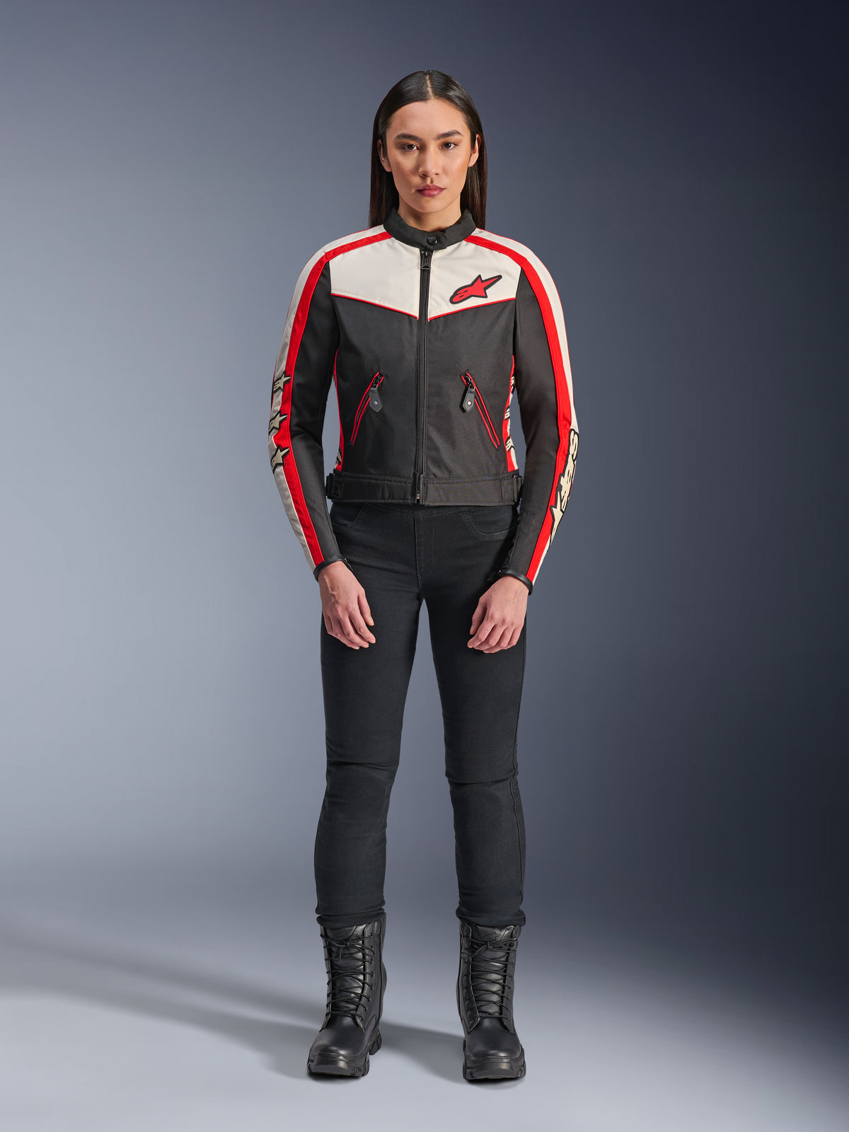 Giacca Alpinestars Stella T-Dyno WR, giacca da moto in tessuto da donna, nero, ecru e rosso acceso, indossata da una modella con pantaloni e stivali neri, caratterizzata da un design d'ispirazione vintage con logo Alpinestars rosso e pannelli a contrasto.