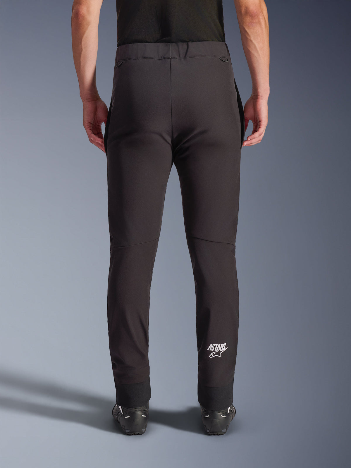 Alpinestars Aeroshell Pants, pantaloni da moto in softshell neri, vista posteriore con vestibilità slim e ginocchia pre-curvate, logo Astars bianco sul polpaccio inferiore destro, orlo elasticizzato, design crossover per uso stradale