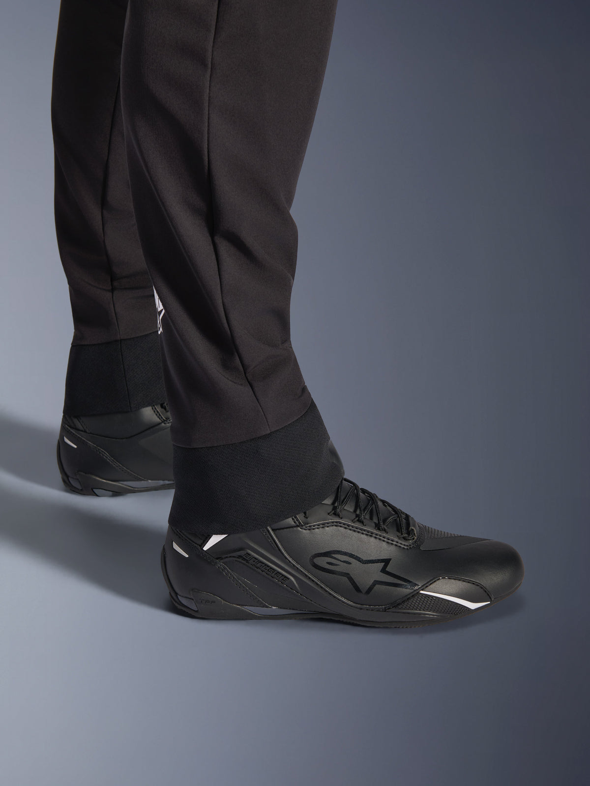 Pantaloni Alpinestars Aeroshell, neri, vista ravvicinata dell'orlo inferiore e del polsino elasticizzati, design moderno in softshell sportivo, indossati con scarpe da moto Alpinestars nere.