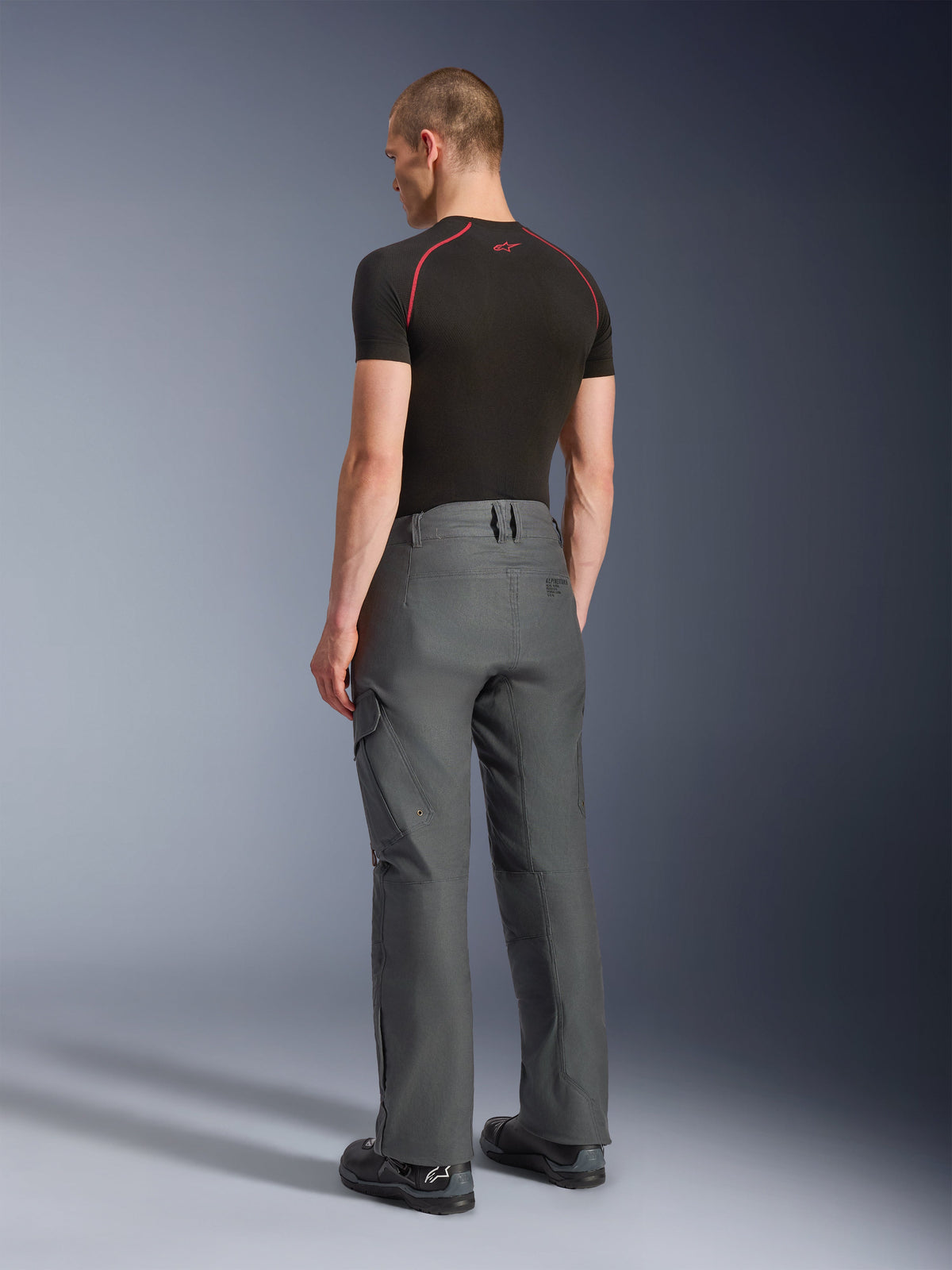 Alpinestars Borrego Drystar® Pants, pantaloni da moto adventure, grigio antracite, vista posteriore, con look in tela cerata e tasche cargo, abbinati a una t-shirt nera e stivali da moto, design resistente per road e adventure touring