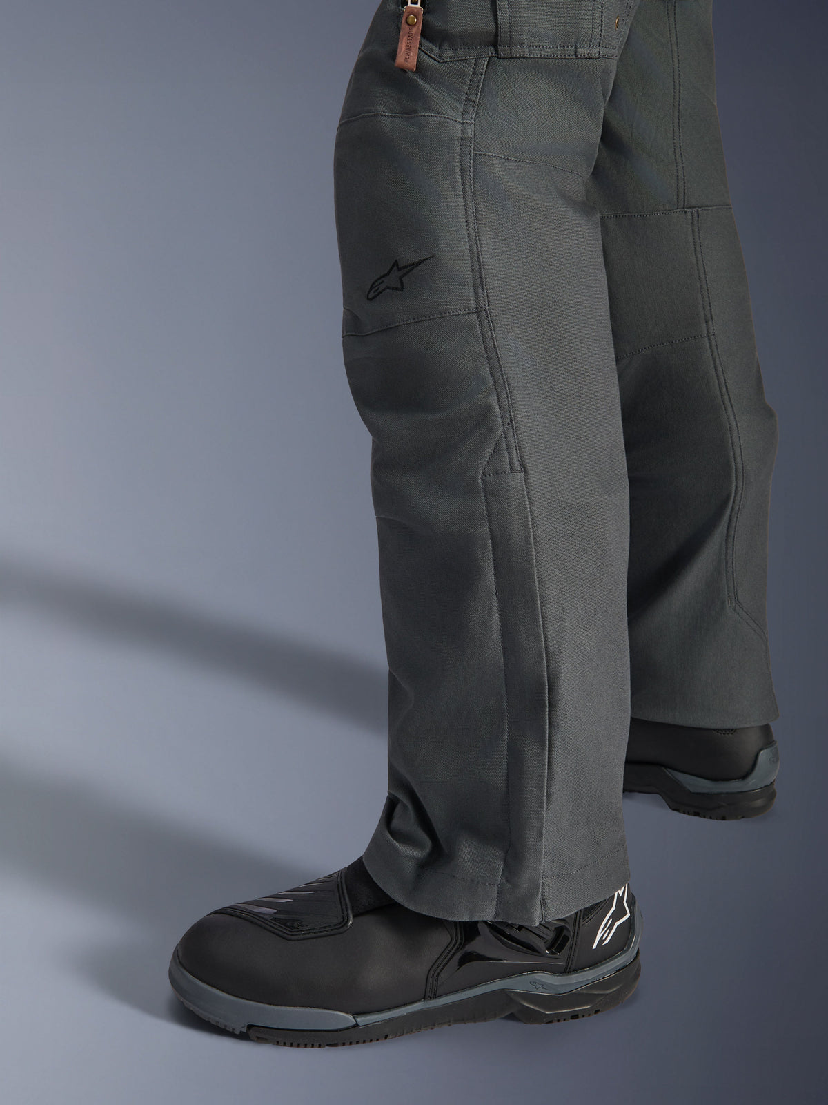 Pantaloni Alpinestars Borrego Drystar®, pantaloni da moto adventure grigio antracite con un aspetto in tela cerata, costruzione in tessuto vista di lato con stivali da moto neri, design robusto per strada e adventure touring